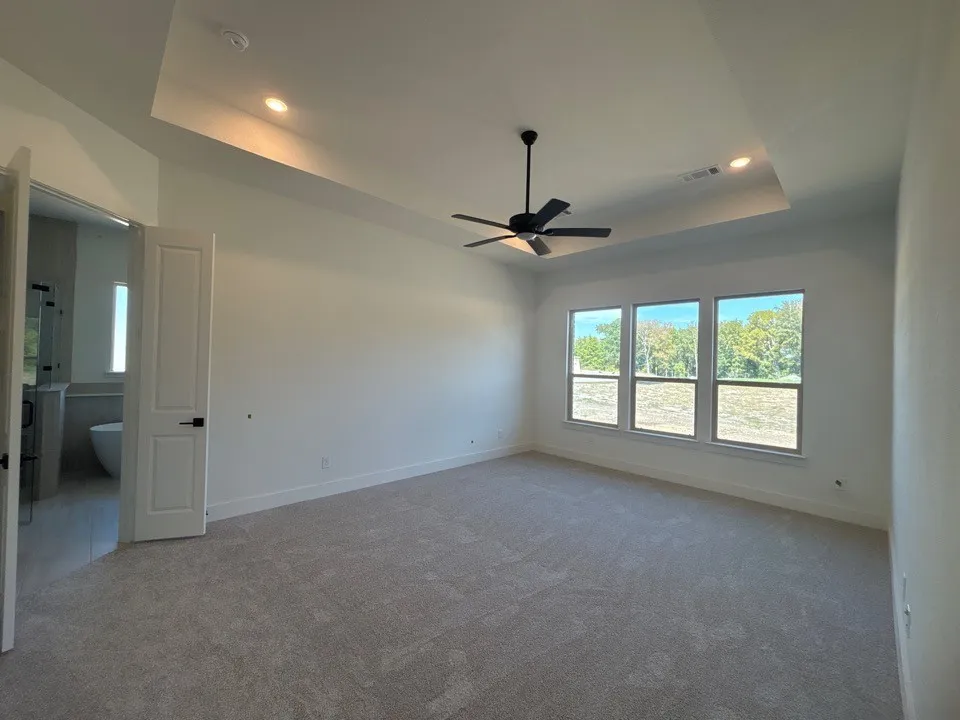 Tray ceiling with recessed lighting, three large windows, ceiling fan, and carpeted flooring