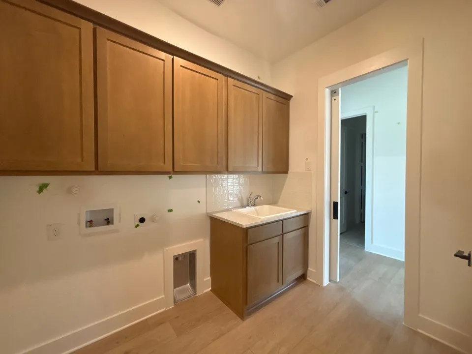 Wood-finish flooring, shaker-style cabinetry, and a utility sink with a white tile backsplash