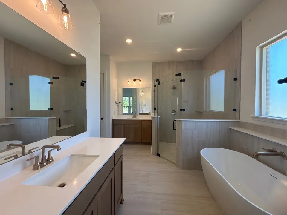 Dual vanities with undermount sinks, a freestanding soaking tub, a frameless glass shower enclosure, and wood-finish tile flooring