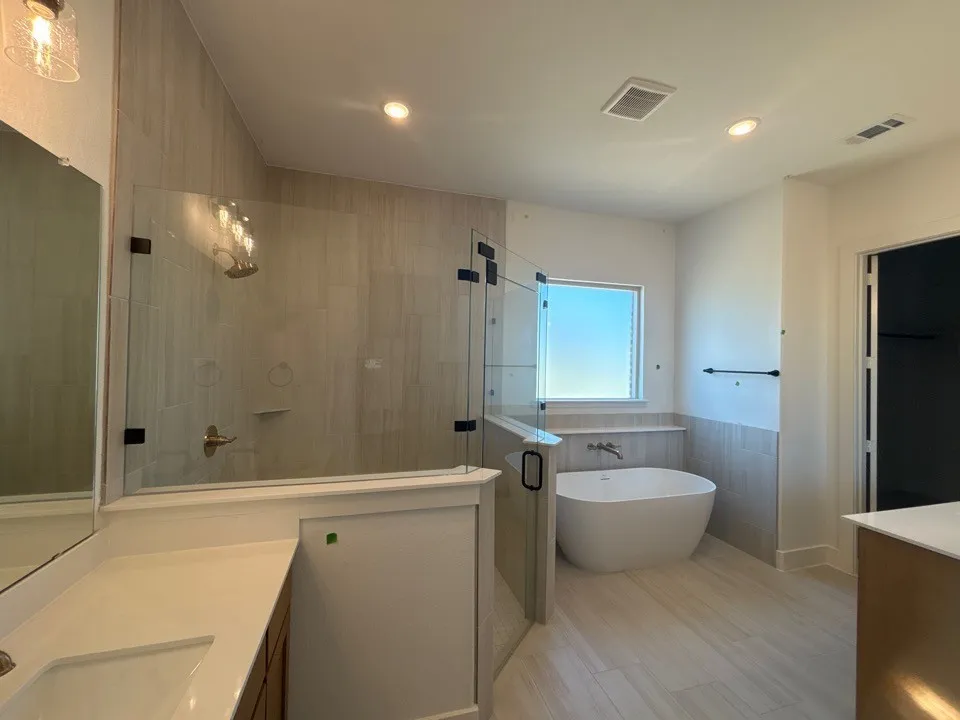 White freestanding soaking tub, clear glass shower enclosure, tiled shower walls, wood-finish flooring, and a window with natural light