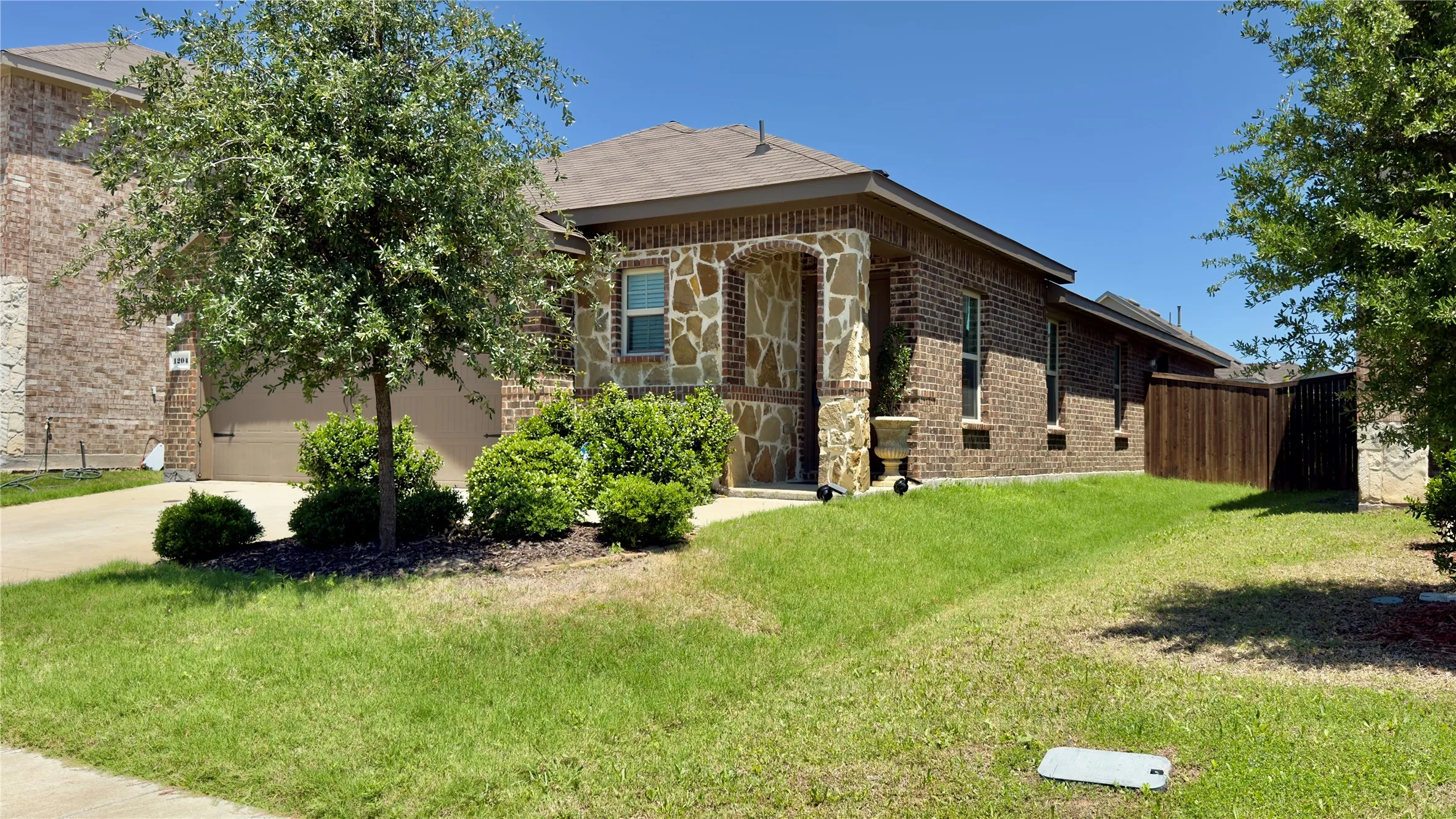Brick and stone facade residence featuring an attached garage, a covered entryway, and a private wooden fence