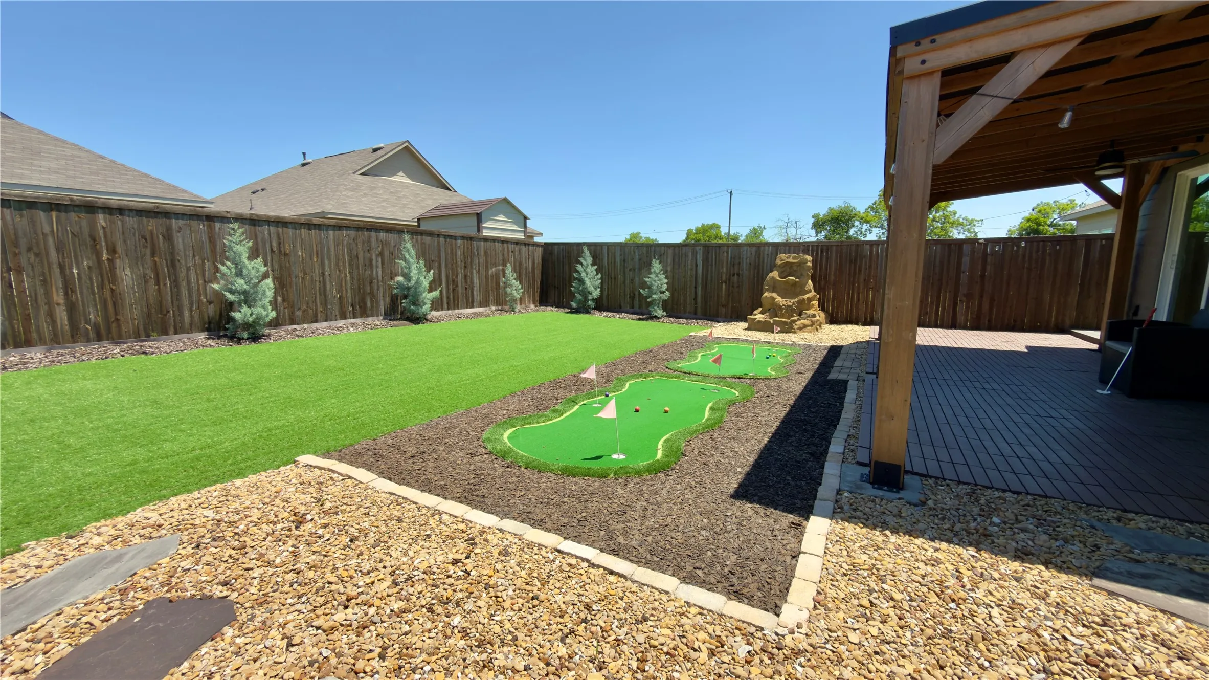 Expansive backyard featuring artificial turf, a putting green, and a rock water feature