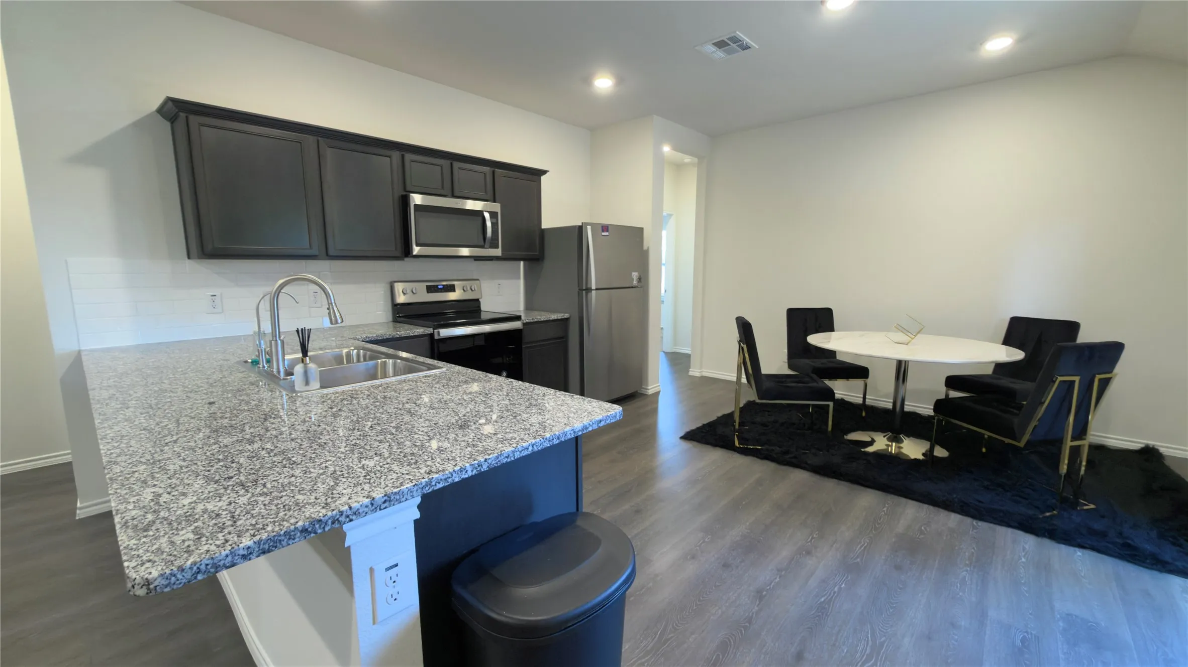 Kitchen featuring a granite-top island with an undermount double sink, dark cabinetry, stainless steel appliances, and wood-finish flooring