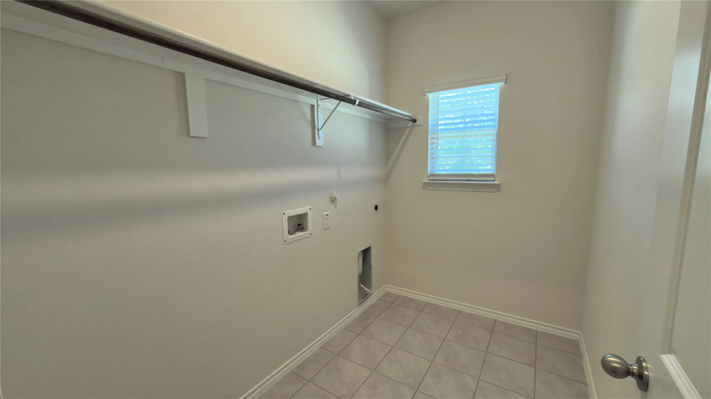 Laundry room featuring tiled flooring, a single window with blinds, a clothes hanging rod, and wall hookups for appliances