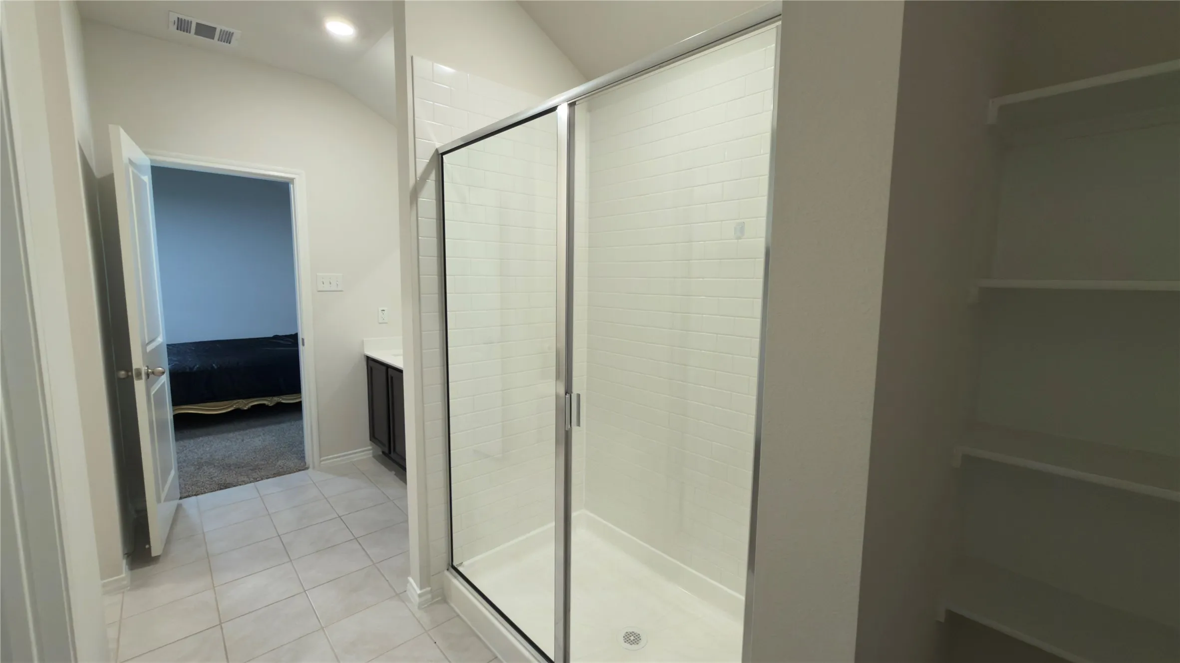 Glass-enclosed shower with subway tile surround, featuring light-toned tile flooring, recessed lighting, and built-in shelving