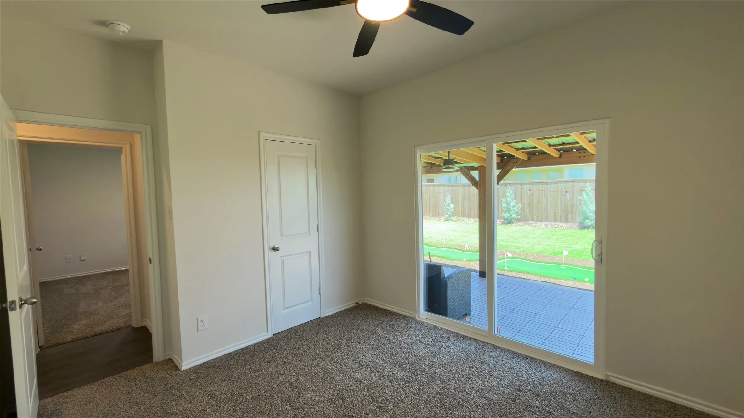 Carpeted interior space featuring a ceiling fan with integrated lighting, a panel door, and a sliding glass door opening to a tiled patio