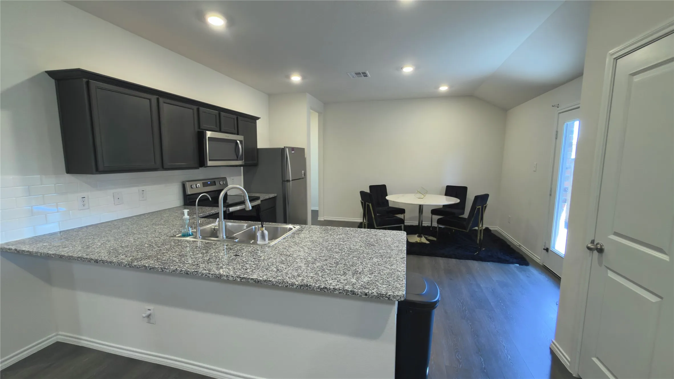 Open-concept kitchen and dining area featuring granite countertops, dark wood-finish cabinetry, stainless steel appliances, and wood-finish flooring