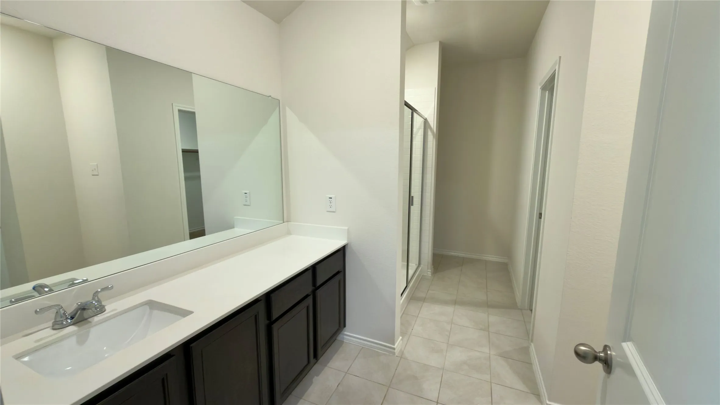 Bathroom featuring a white countertop with an integrated sink, dark wood-finish cabinetry, a large wall-mounted mirror, and tile flooring