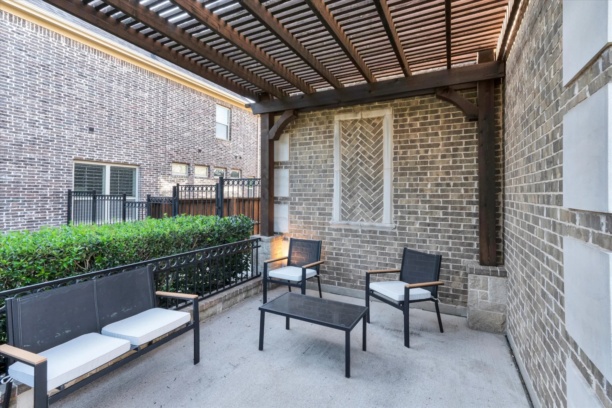 Paved patio area featuring a slatted wood pergola, brick exterior walls, and a decorative brick window accent