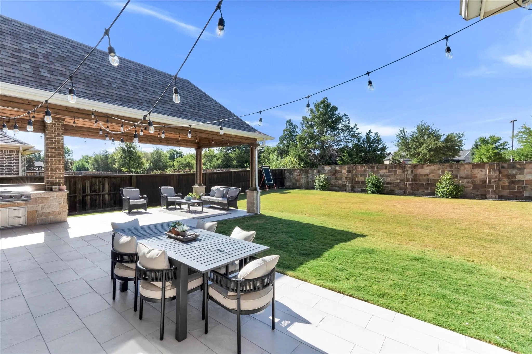 Expansive backyard featuring a covered patio, outdoor kitchen, string lighting, and a large lawn area