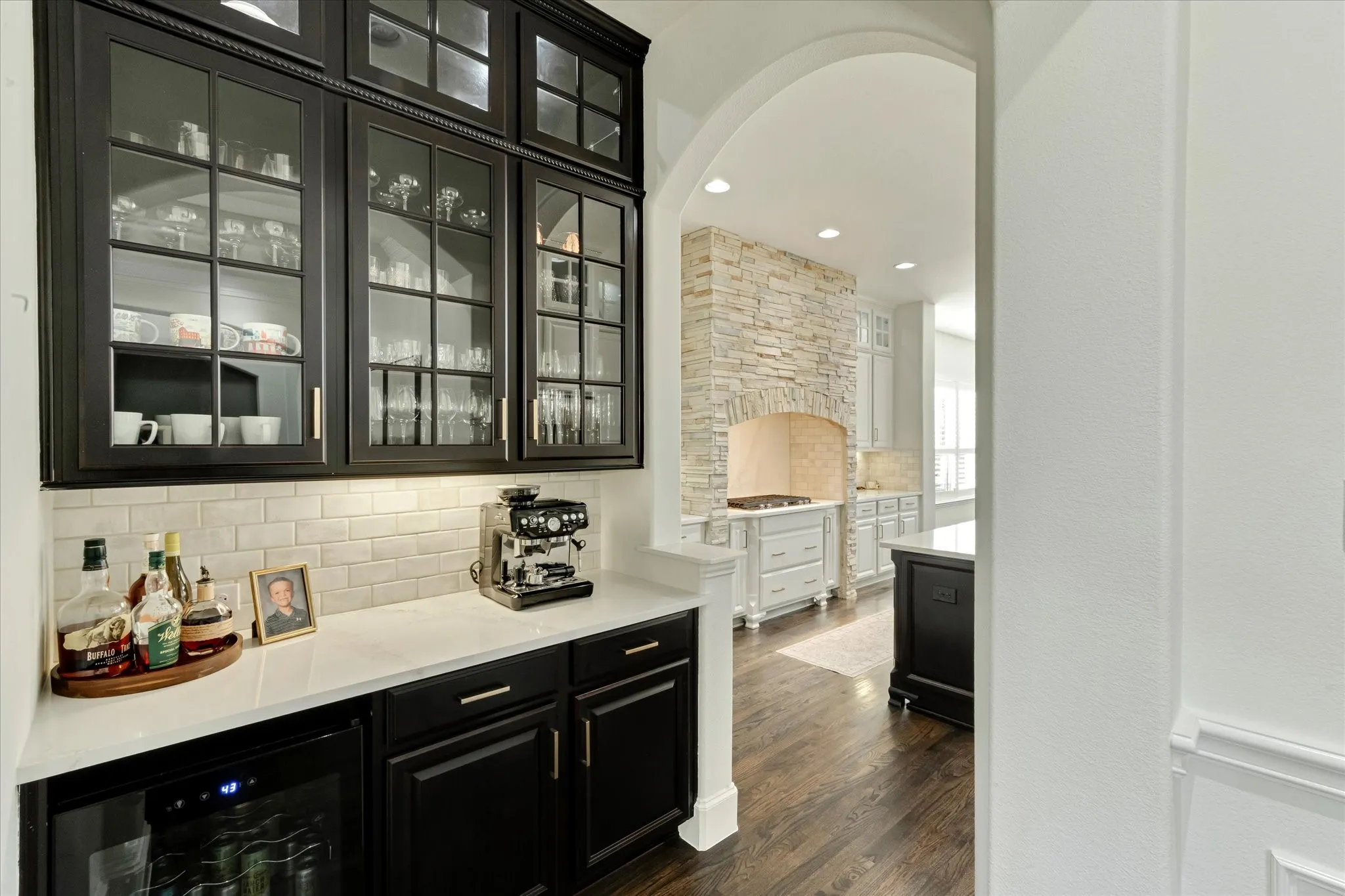 Built-in cabinetry with glass-front uppers, solid surface countertop, subway tile backsplash, and under-cabinet lighting