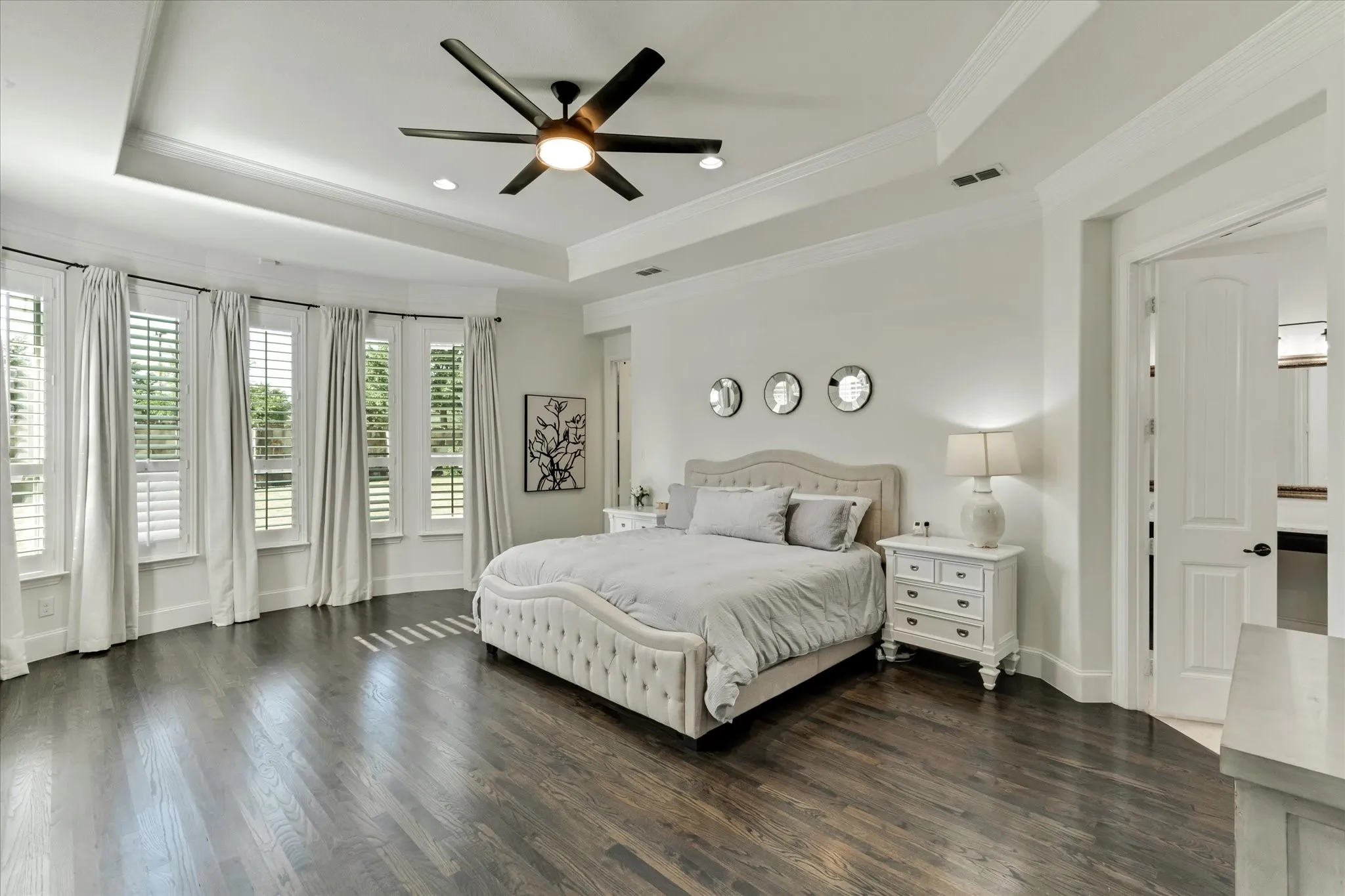 Dark wood-finish flooring with a multi-pane bay window, white plantation shutters, and recessed lighting