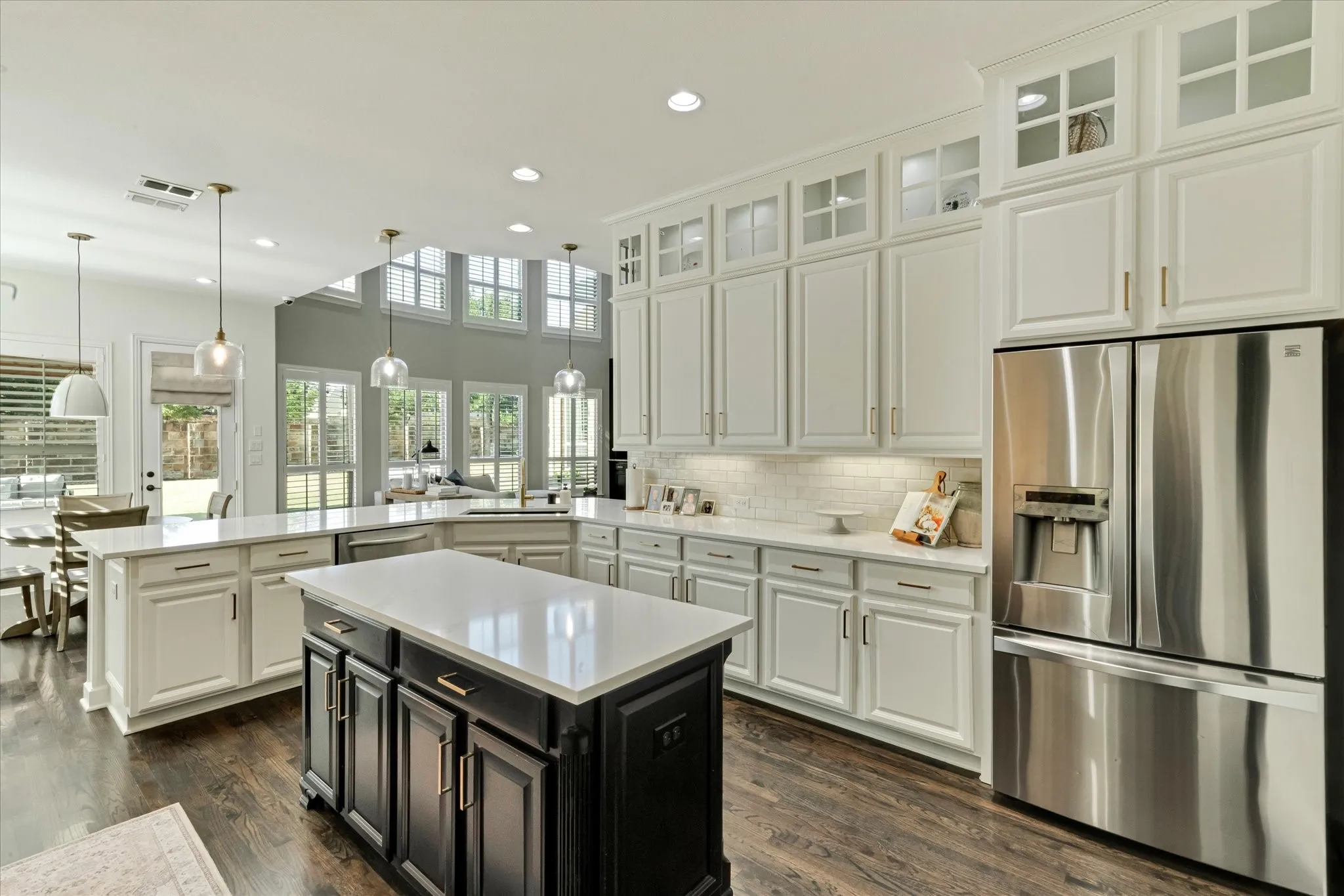 Kitchen featuring a central island, white cabinetry with glass-front uppers, stainless steel French-door refrigerator, subway tile backsplash, and light-toned countertops