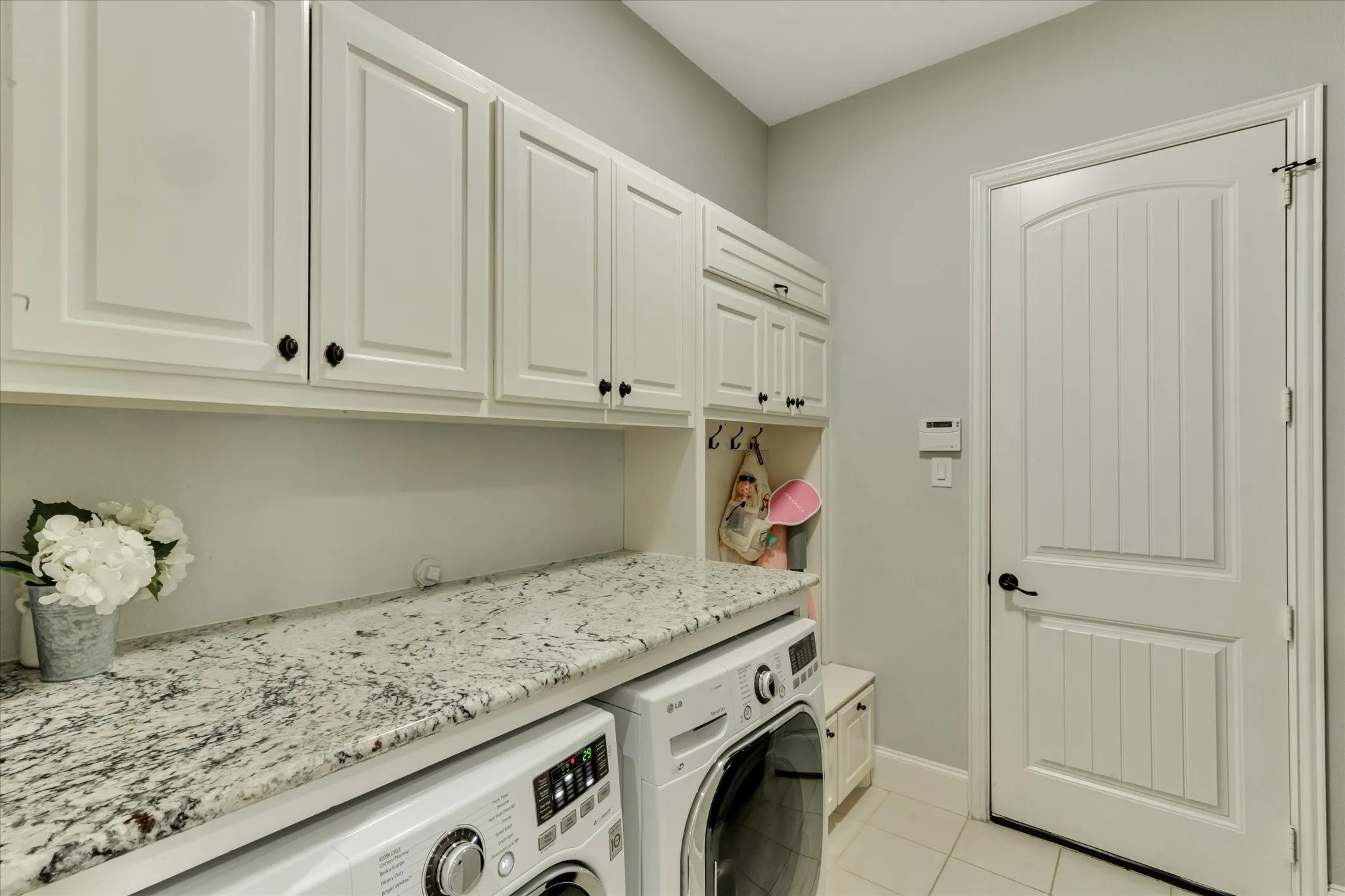 White shaker cabinetry with dark hardware, speckled stone-finish countertop, built-in shelving, paneled door, and tiled flooring