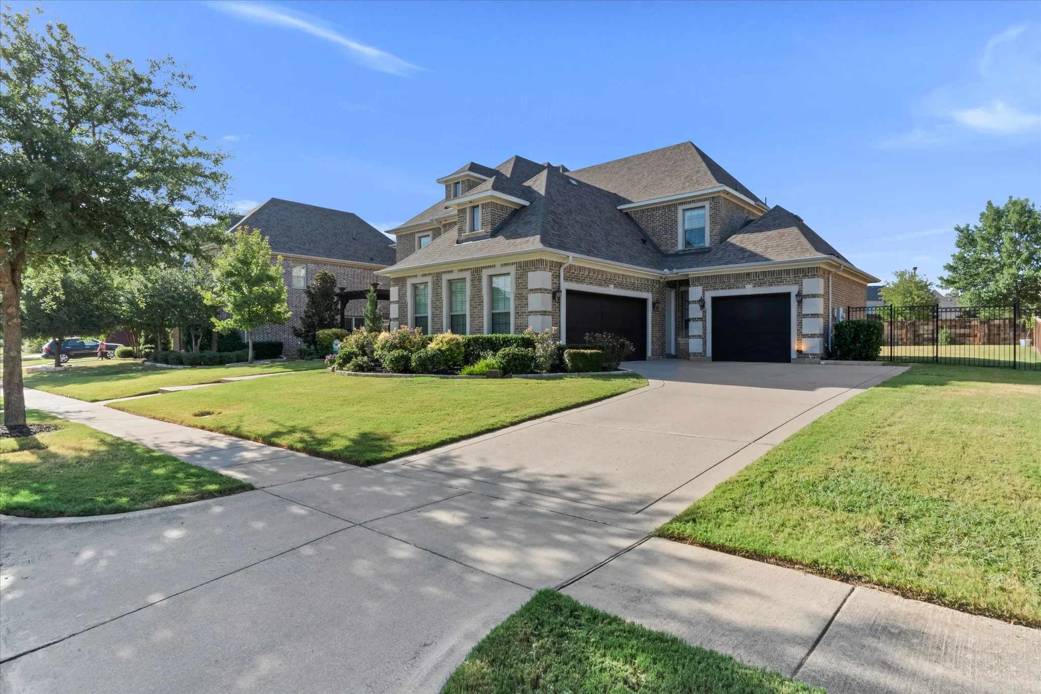 Brick exterior with stone accents, mature landscaping, multi-car garage, concrete driveway, and a fenced perimeter