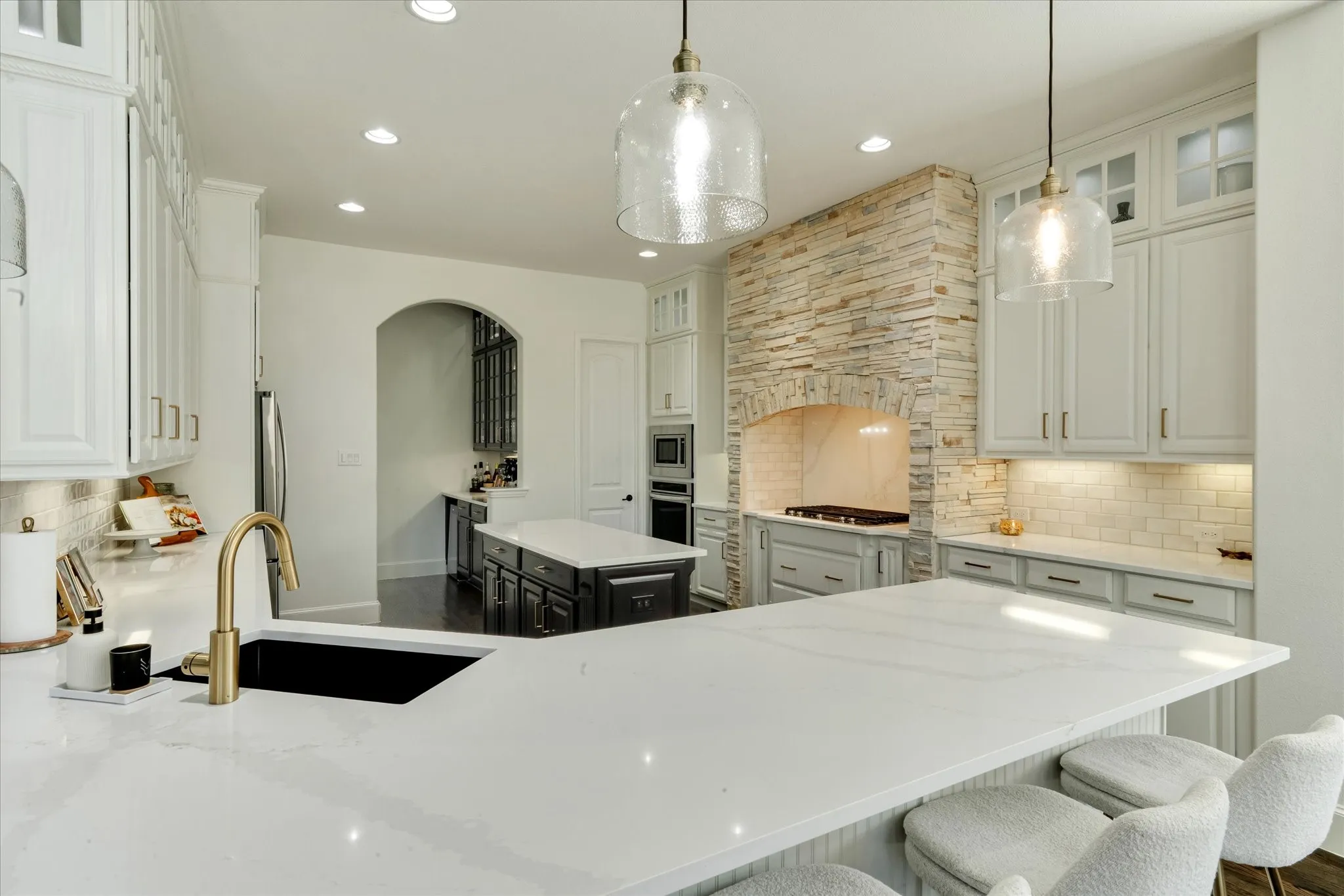 Expansive kitchen featuring white cabinetry, a stone-clad range hood, recessed lighting, and a kitchen island with seating