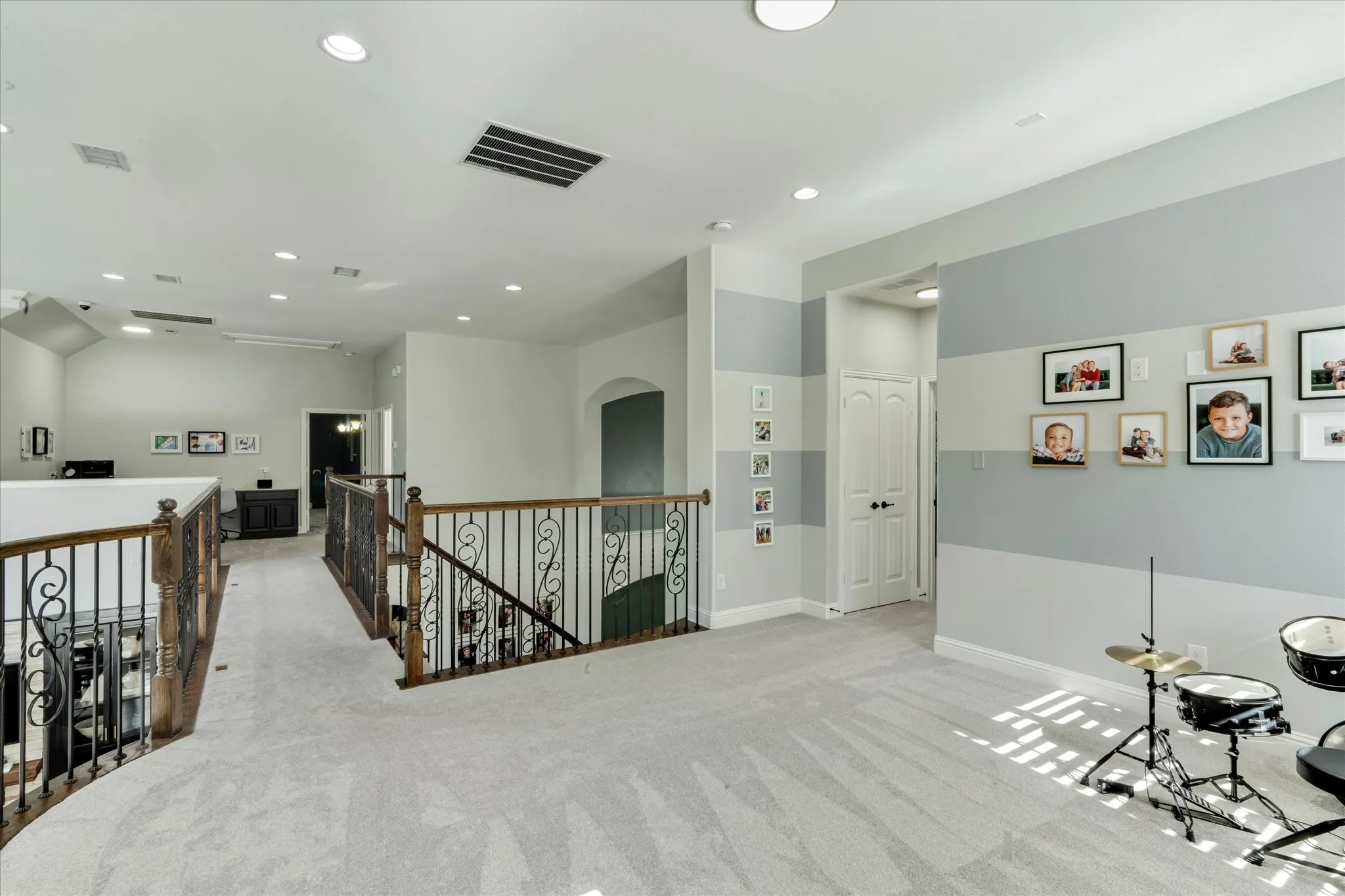 Carpeted landing featuring decorative wrought iron and wood railings, recessed lighting, and a paneled door