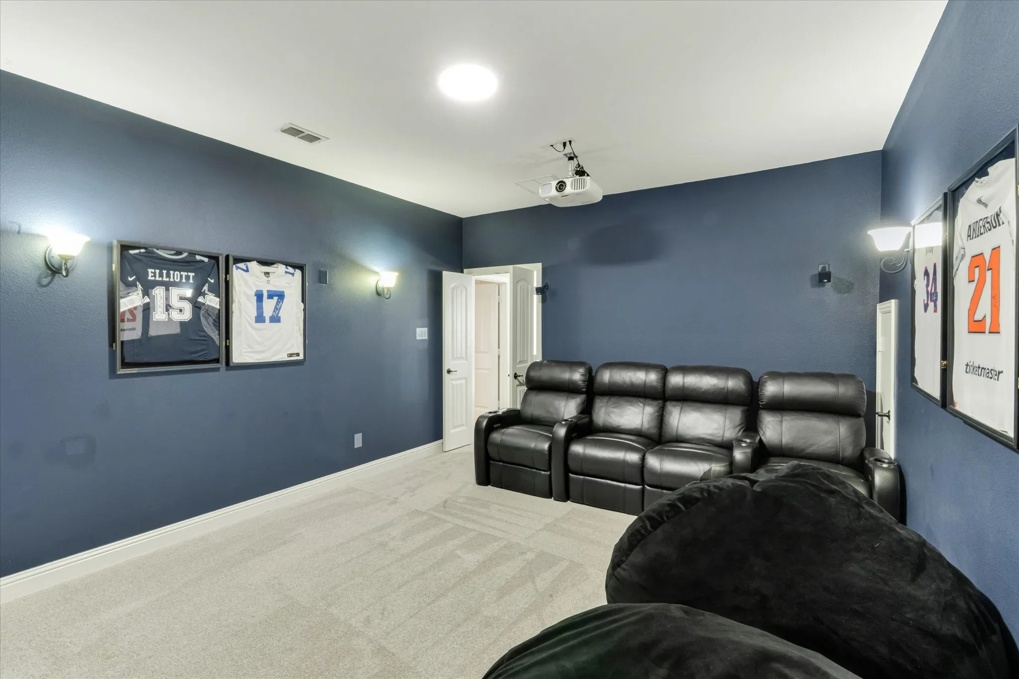 Projector system with ceiling-mounted projector, wall-mounted sconce lighting, and a white ceiling with recessed lighting
