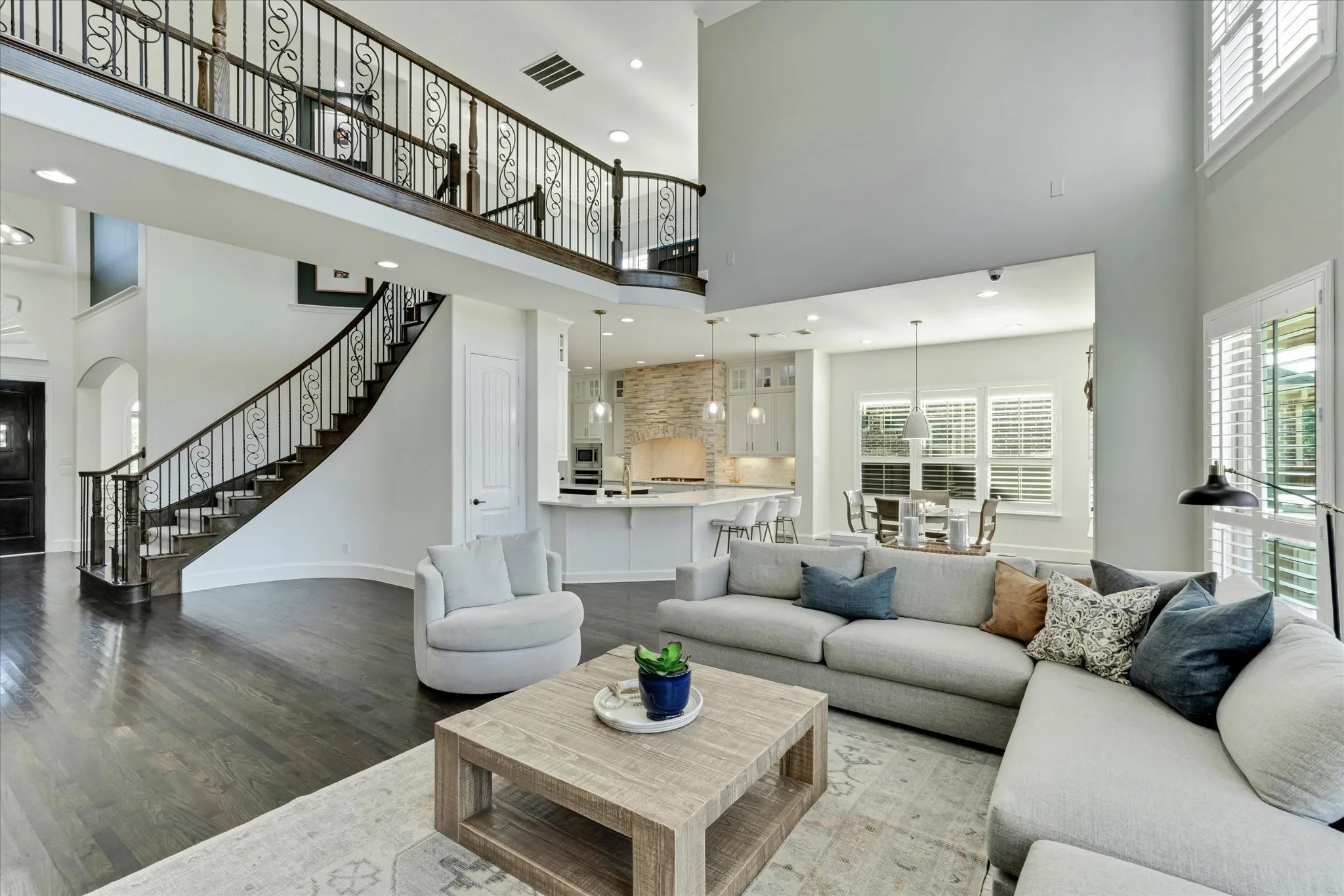 Two-story ceiling height, dark wood-finish flooring, staircase with wrought iron balusters, white plantation shutters, and recessed lighting
