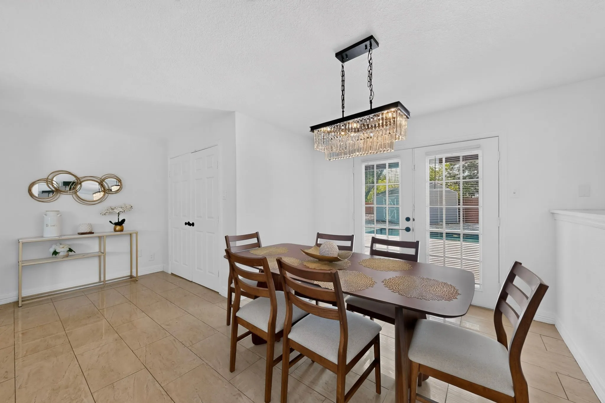 Tiled flooring, white painted walls, a linear crystal chandelier, and exterior French doors