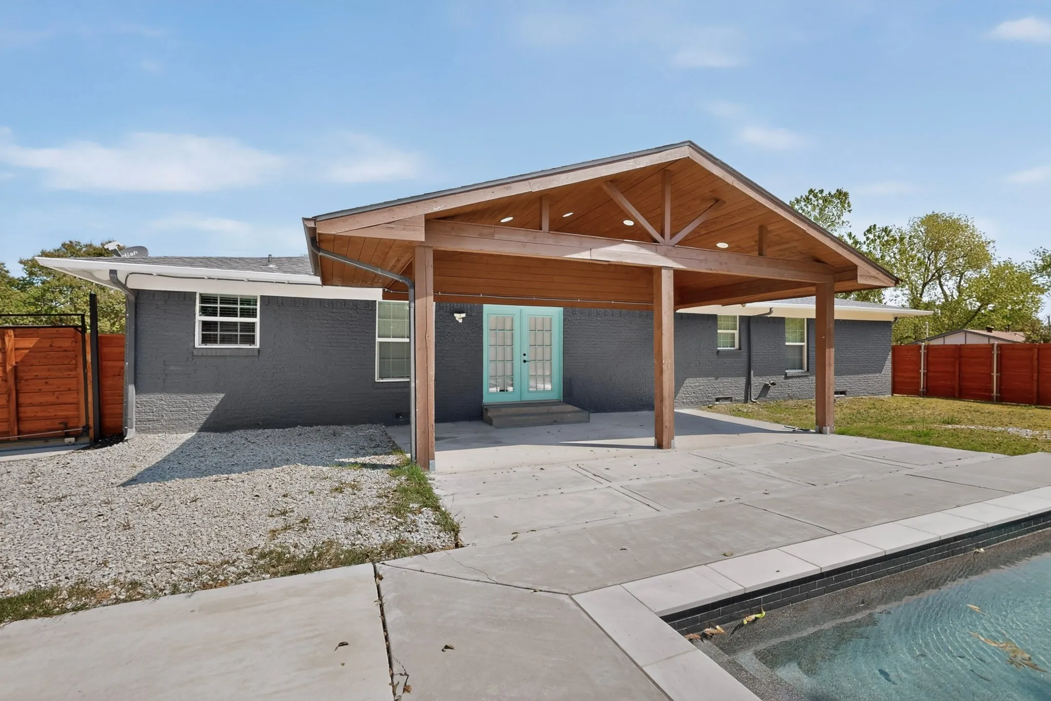 Covered patio with exposed wood beams, concrete patio, light blue French doors, and a swimming pool with dark tile accents