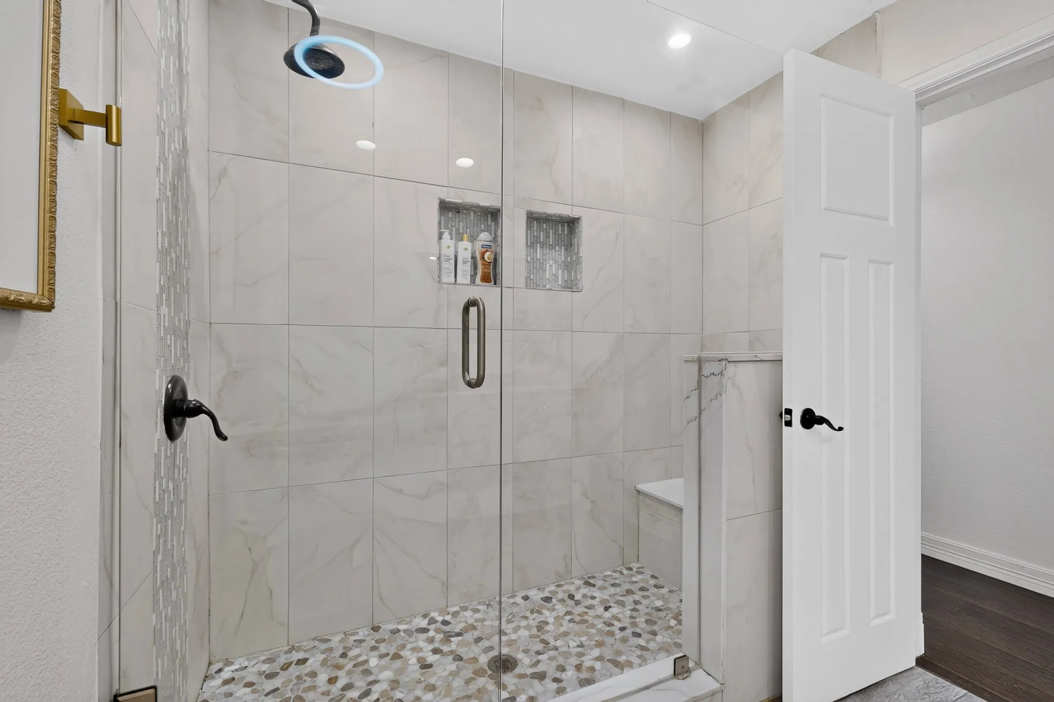 Spacious shower featuring a glass enclosure, pebble-tile flooring, and a built-in bench