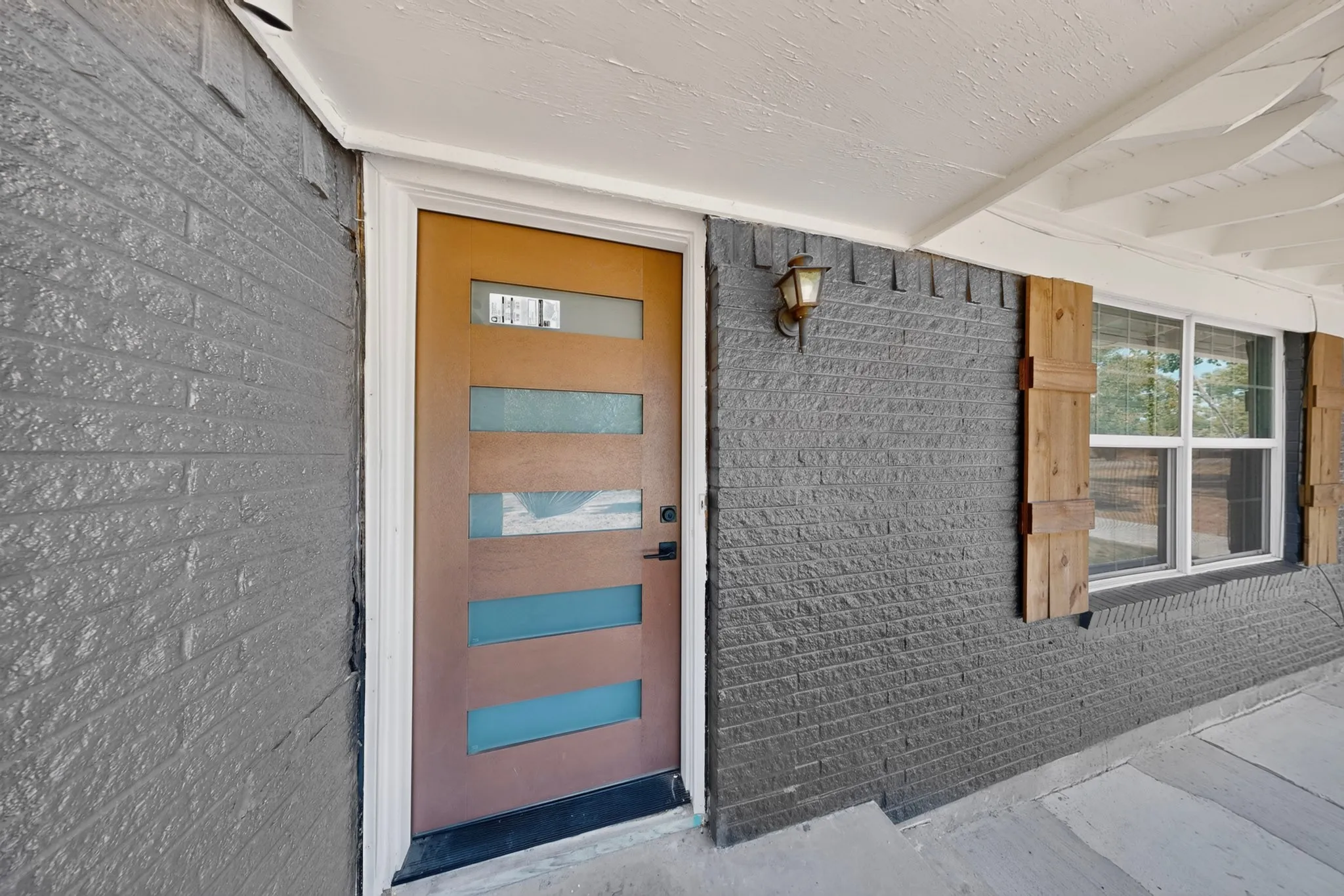 Modern entry door with horizontal frosted glass panes, gray brick exterior, and decorative wood window shutters
