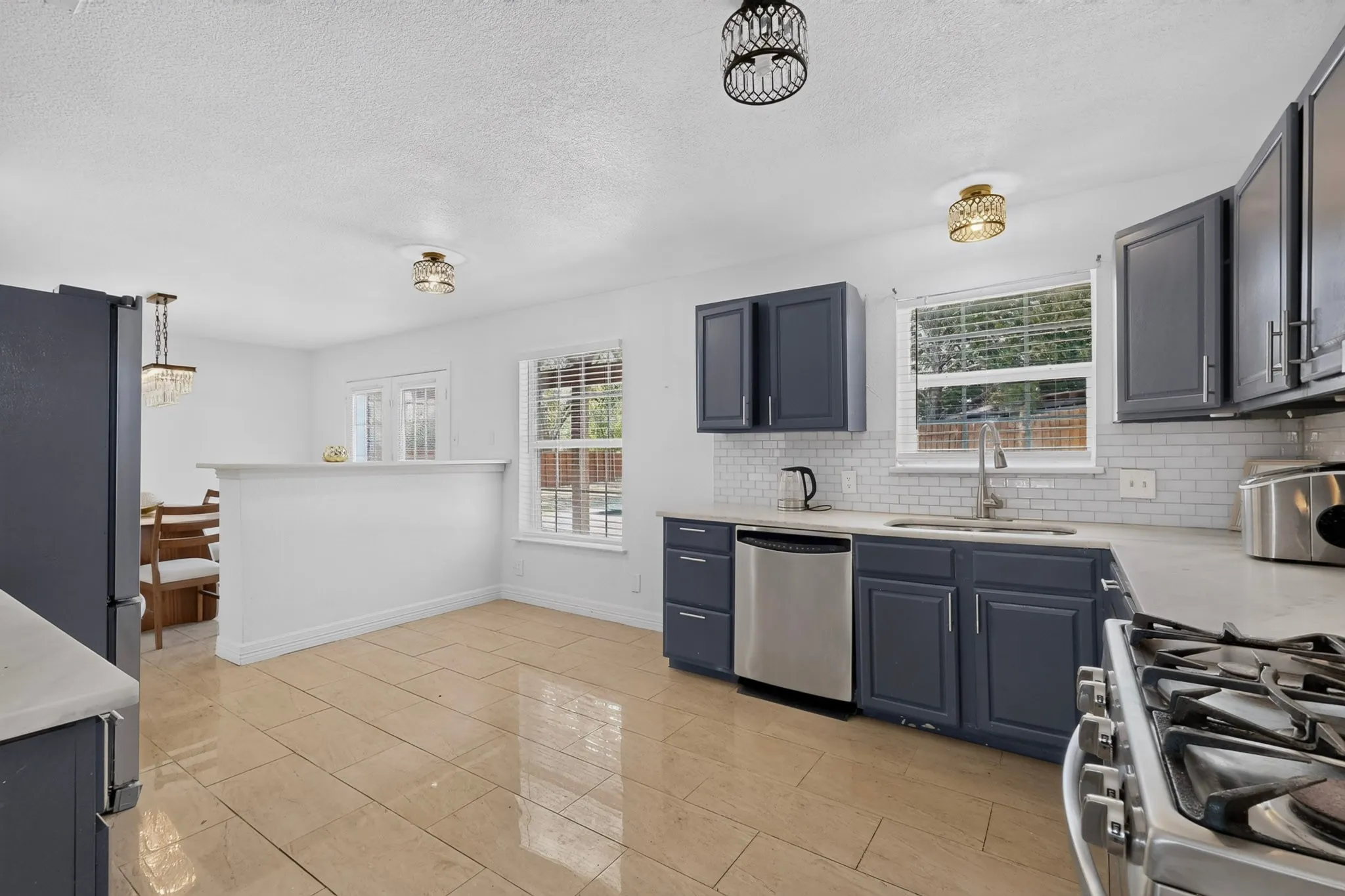 Kitchen featuring dark blue cabinetry, light-toned countertops, subway tile backsplash, stainless steel appliances, and tile flooring