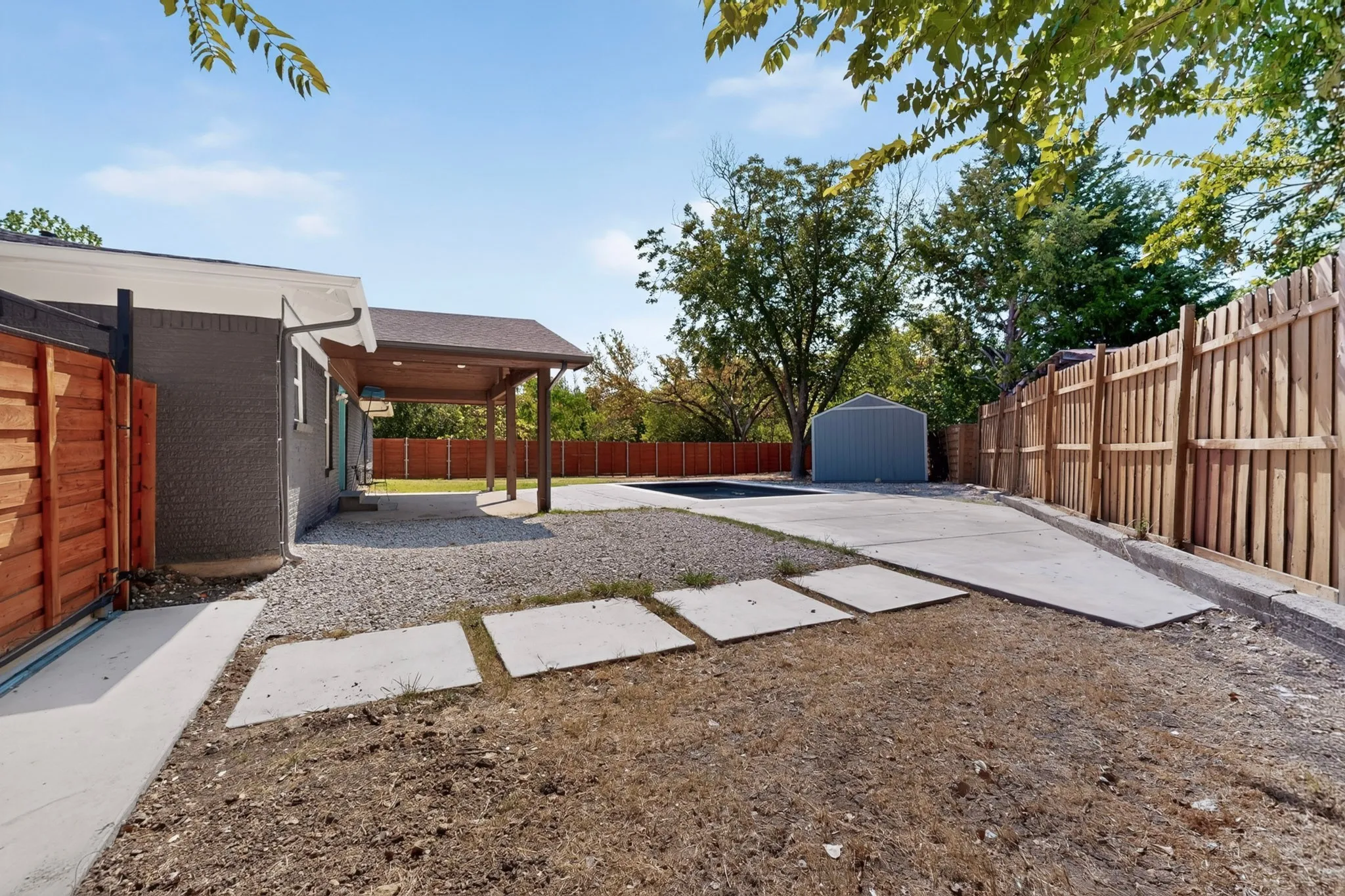 Attached carport with recessed lighting, gravel hardscaping, concrete walkway, and a wooden privacy fence