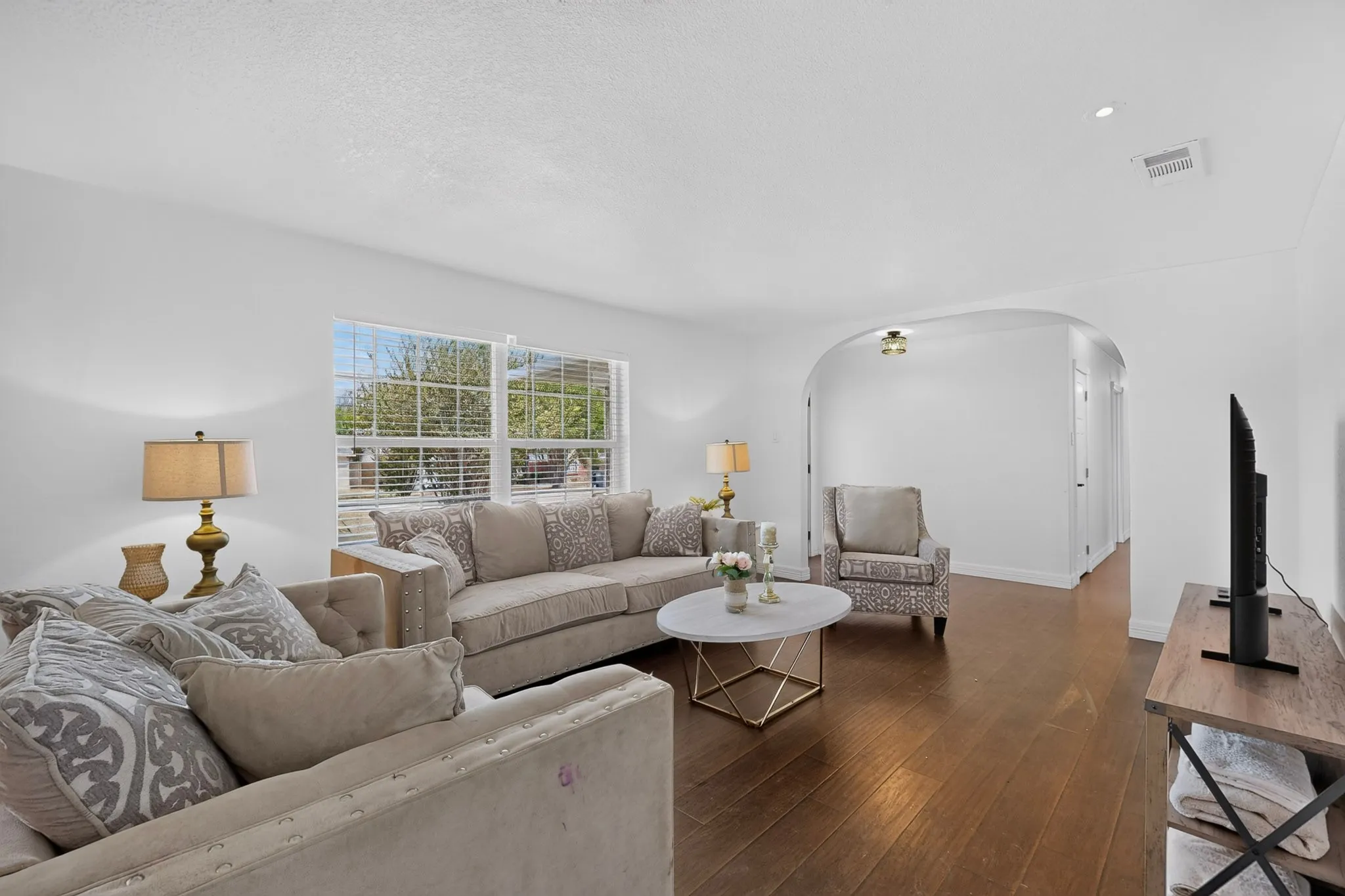 Hardwood flooring throughout, featuring an arched entryway, recessed ceiling lighting, and a window with horizontal blinds