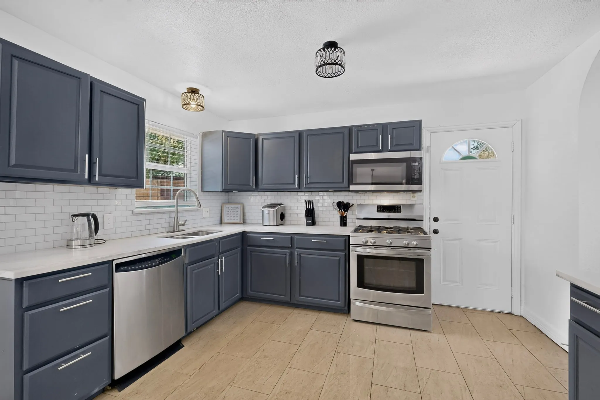 Kitchen featuring slate-toned cabinetry, stainless steel appliances, light-toned countertops, and a subway tile backsplash