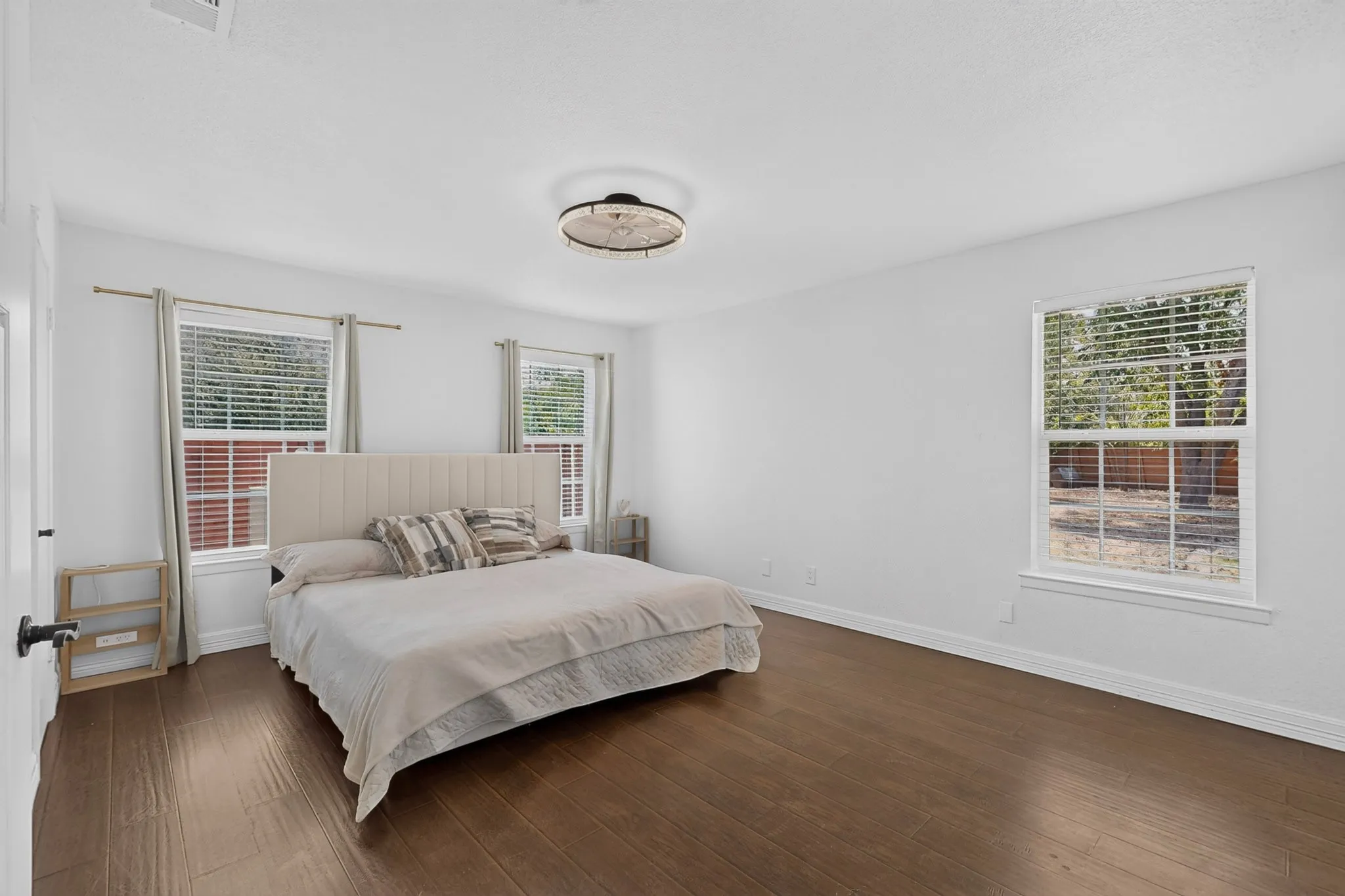 Spacious room featuring wood-finish flooring, multiple windows with blinds, and a contemporary ceiling light fixture