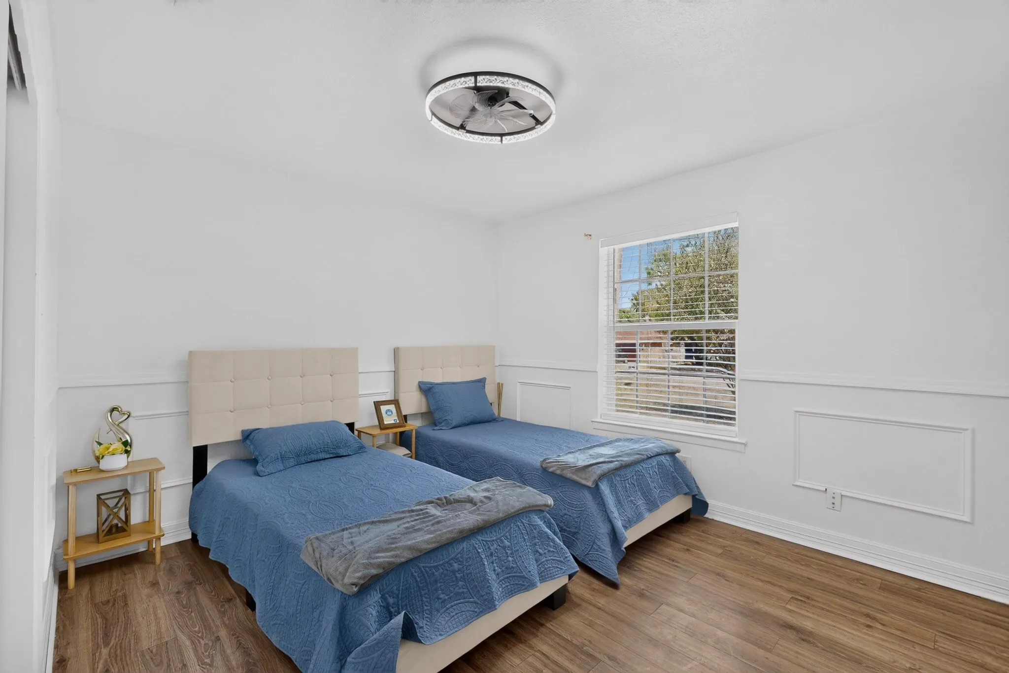 Wood-finish flooring, white walls with wainscoting, and a window with blinds