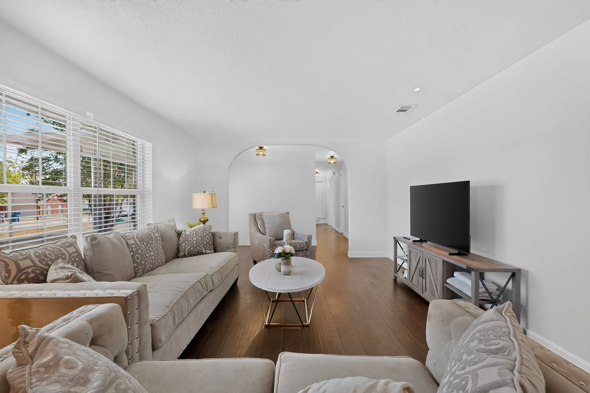 Spacious living area featuring wood-finish flooring, ample natural light from large windows, and an arched doorway