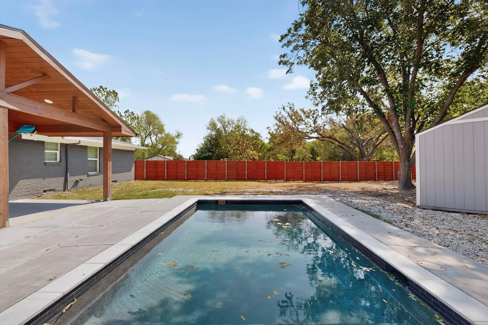 Rectangular swimming pool with gray coping, concrete patio, and a covered patio area with exposed wood beams