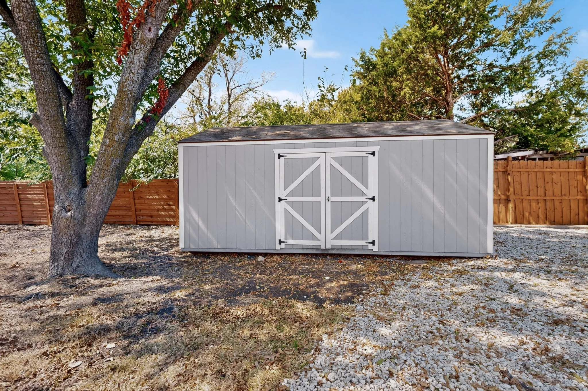 Utility shed with gray siding and white double doors, featuring black hardware and a dark shingle roof