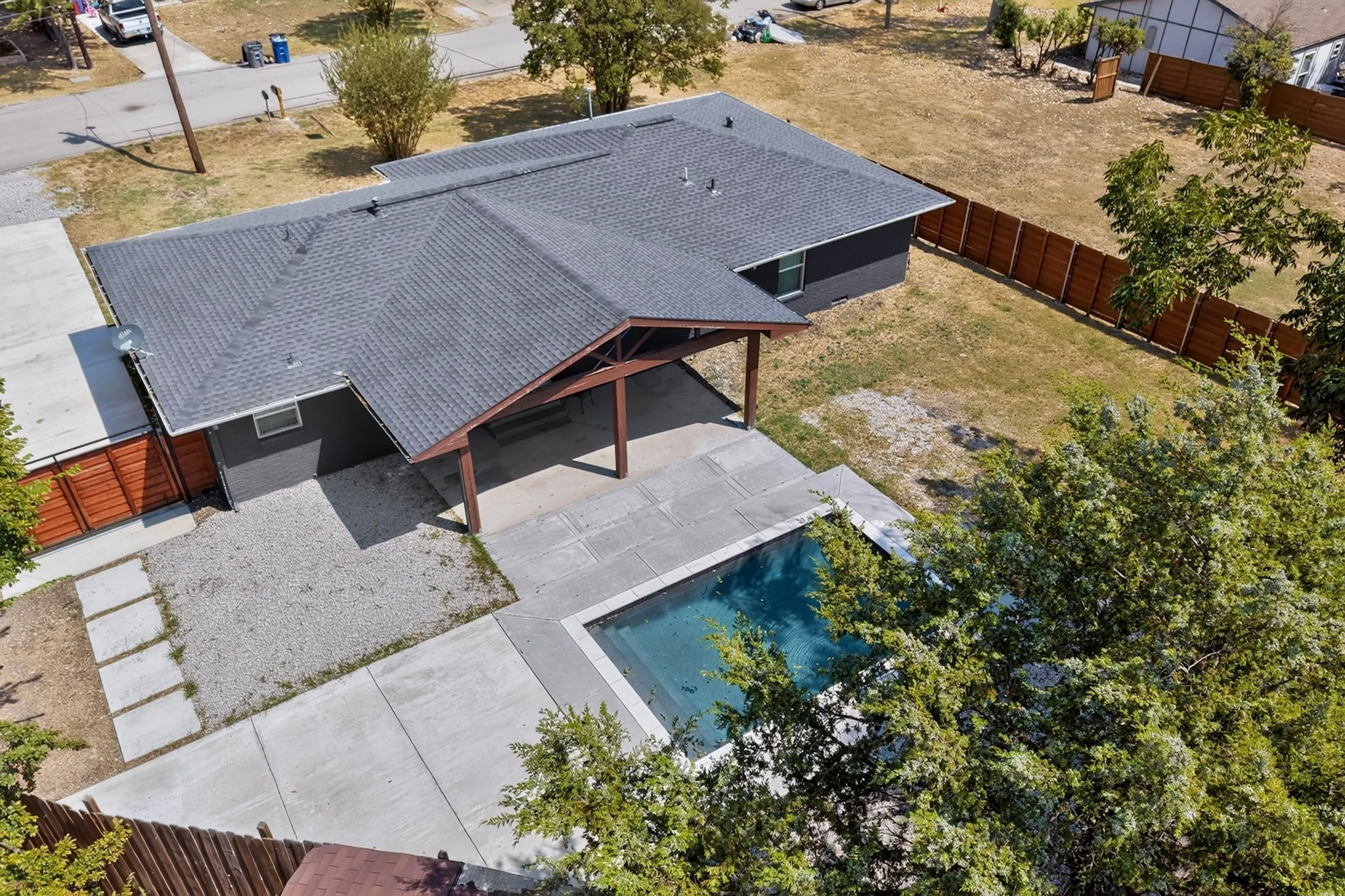 Exterior featuring a dark shingle roof, dark gray siding, an outdoor pool with a concrete surround, and a covered patio with exposed wood beams