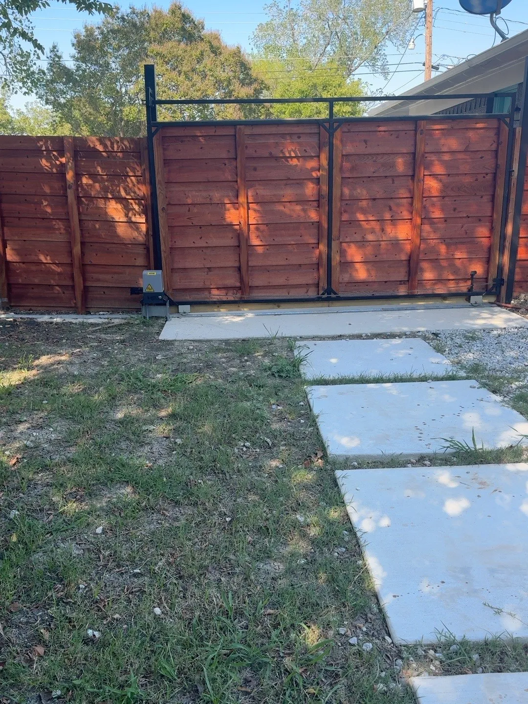 Wood-finish privacy fence with a black metal top rail and automated gate system