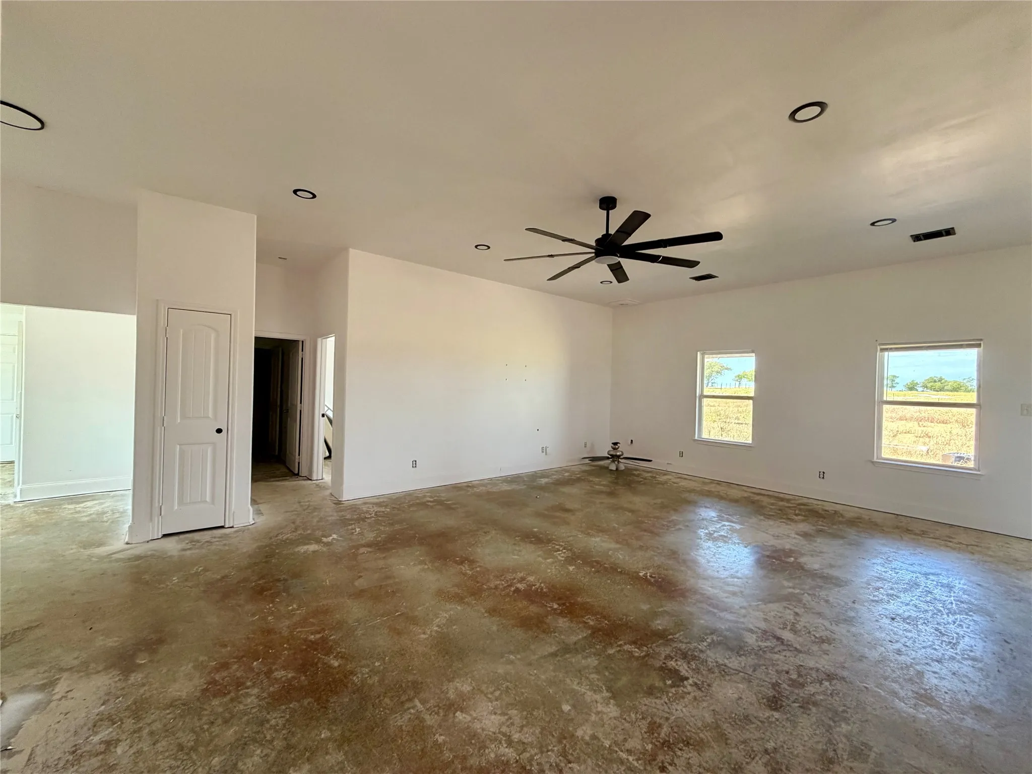 Expansive room with high ceilings, recessed lighting, a ceiling fan, multiple windows, and stained concrete flooring. Beautiful views through the many windows.