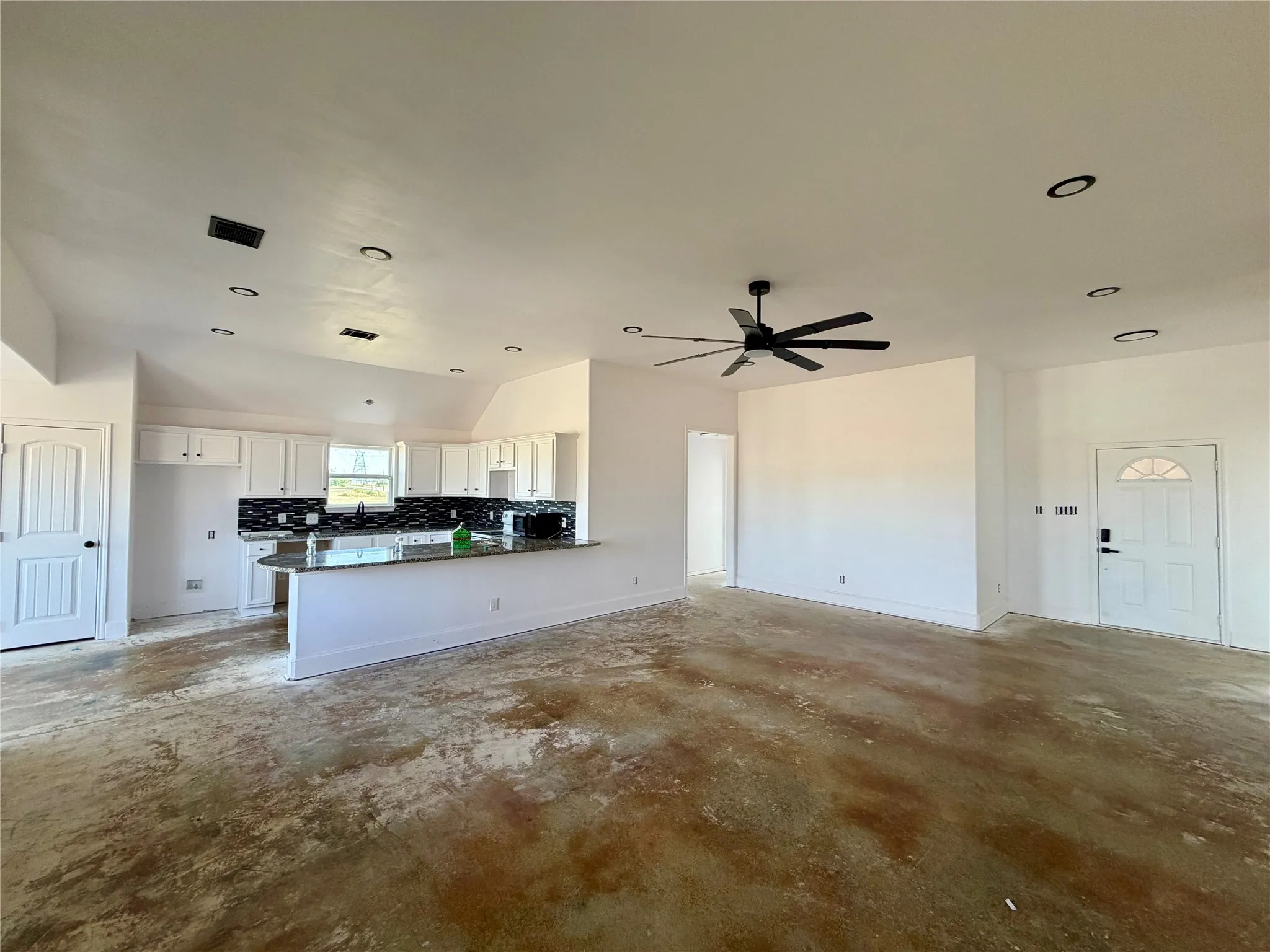 Open-concept living space featuring a kitchen with a breakfast bar, fresh white cabinetry, lots of recessed lighting, and an oversized ceiling fan
