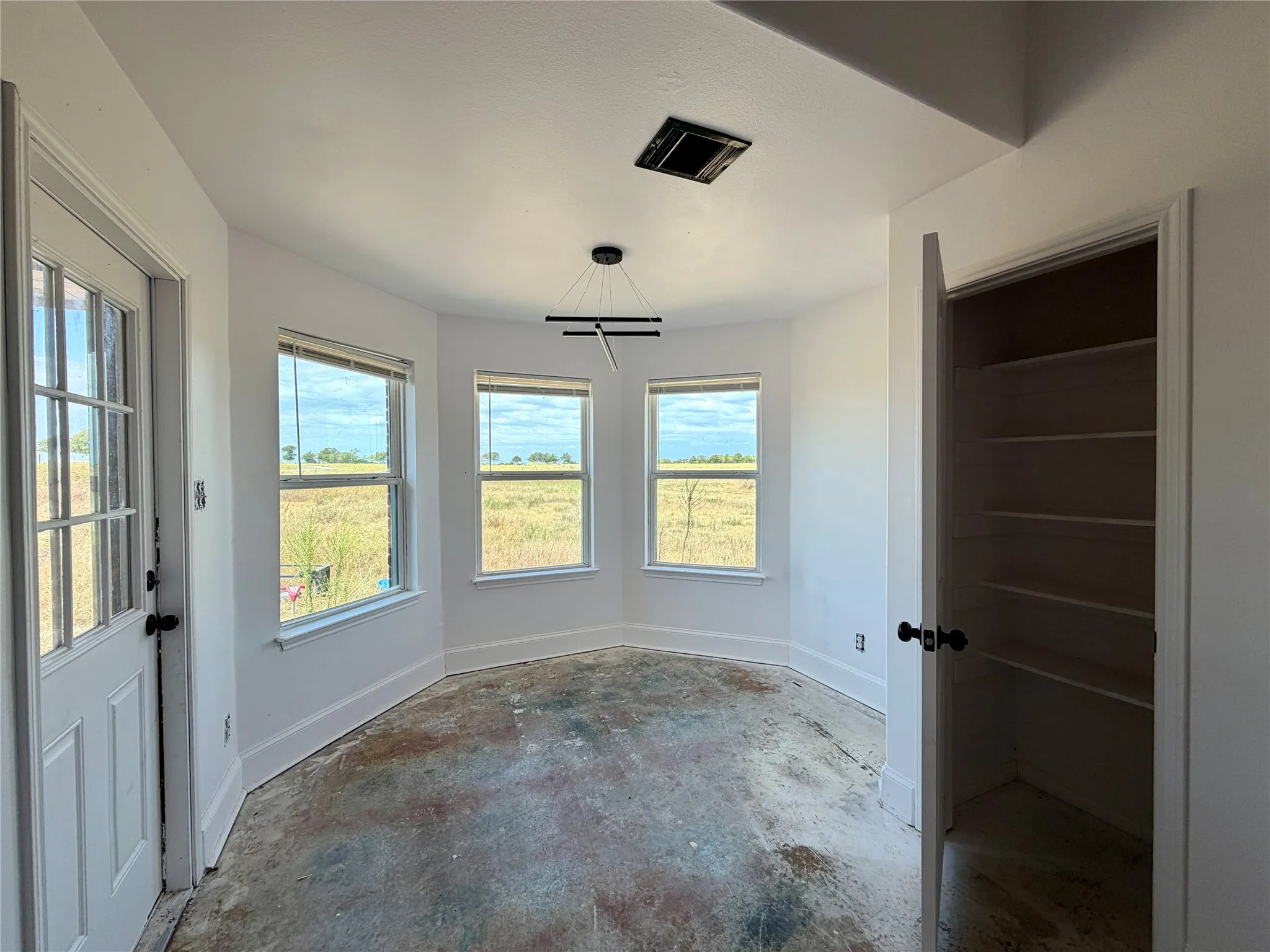 Bay window alcove for your dining area. a modern linear pendant light fixture, tall baseboards.  Beautiful view of the backyard.  Notice the open door to the spacious kitchen pantry to your right.