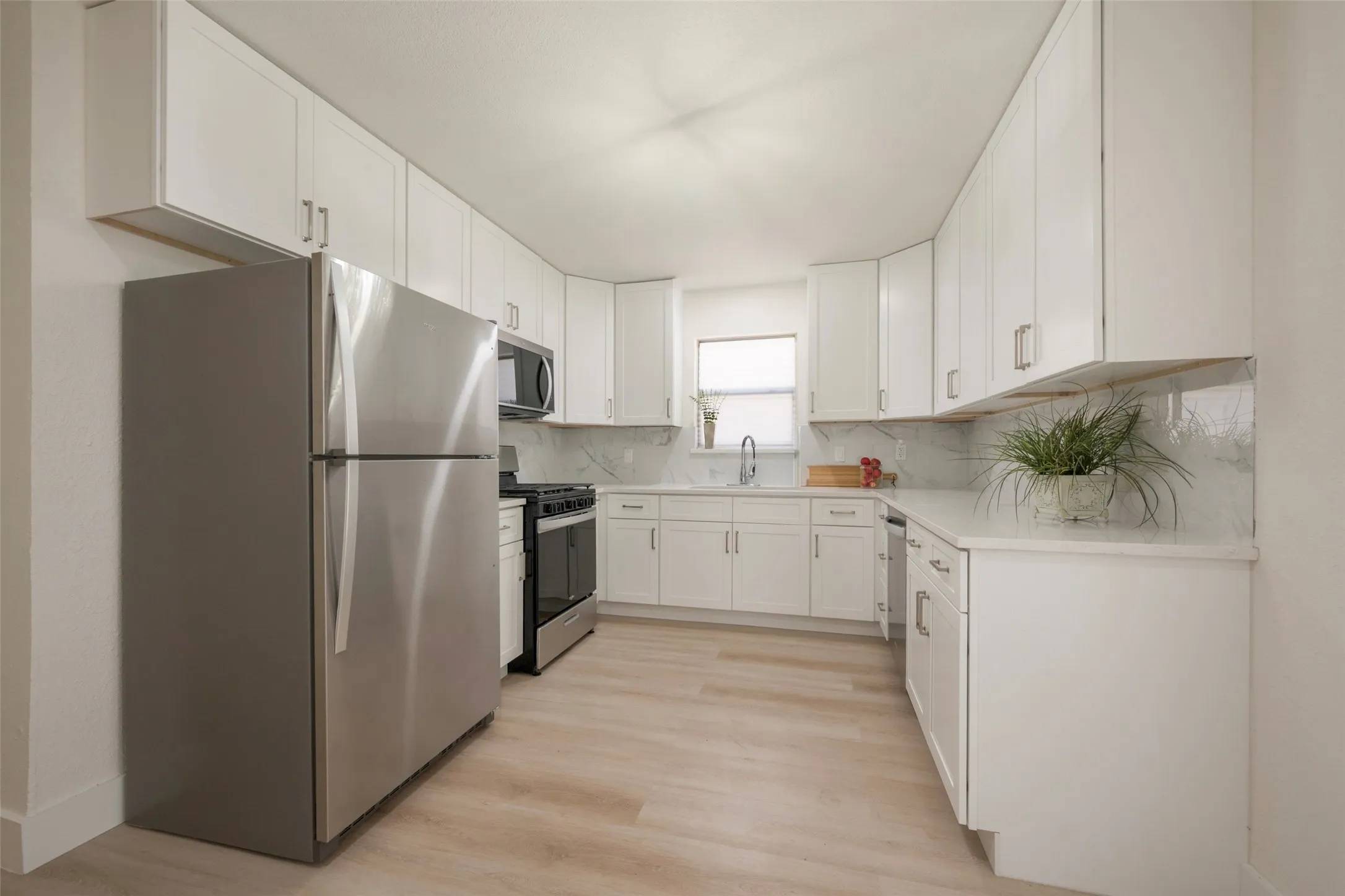 Updated kitchen featuring white shaker cabinetry, stainless steel appliances, light wood-finish flooring, white countertops, and a tile backsplash