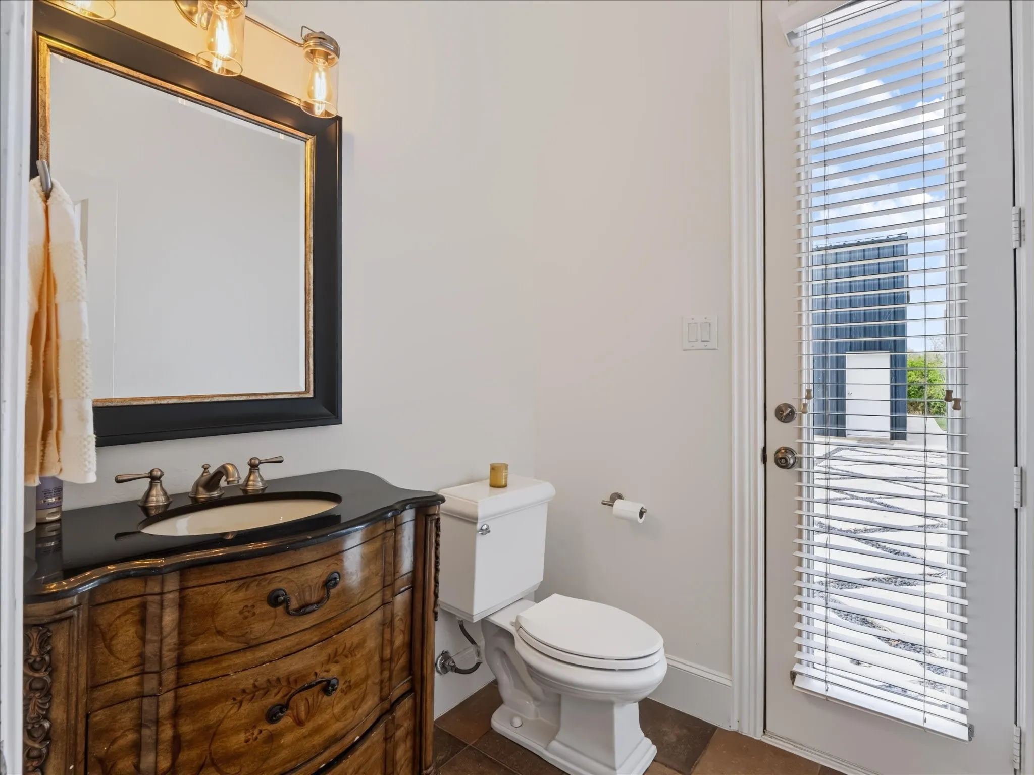 Vanity with dark countertop and integrated sink, bronze-finish faucet, and coordinating wall-mounted light fixture