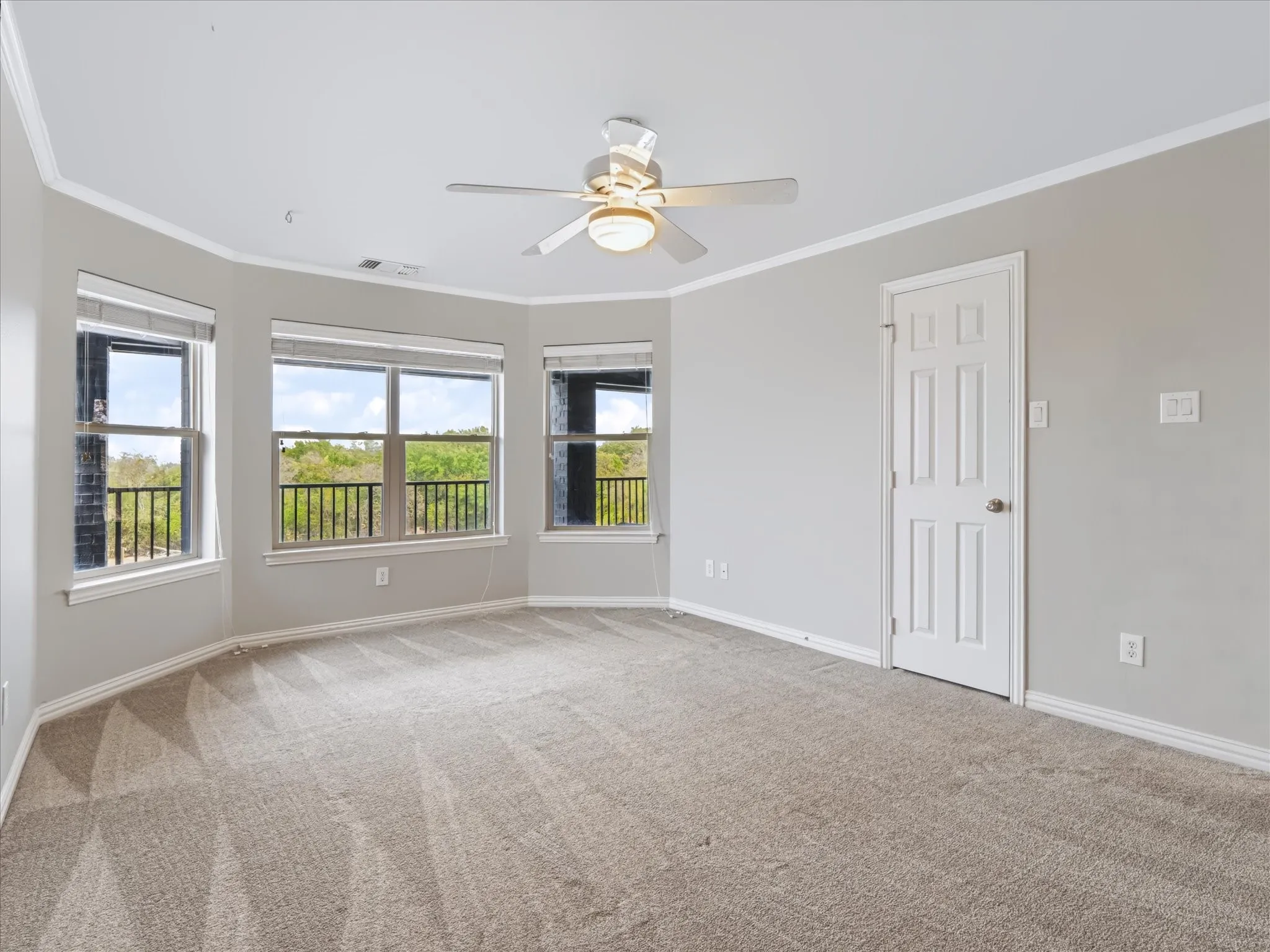 Recessed bay window design, crown molding, ceiling fan with integrated lighting, paneled interior door, and textured carpet flooring