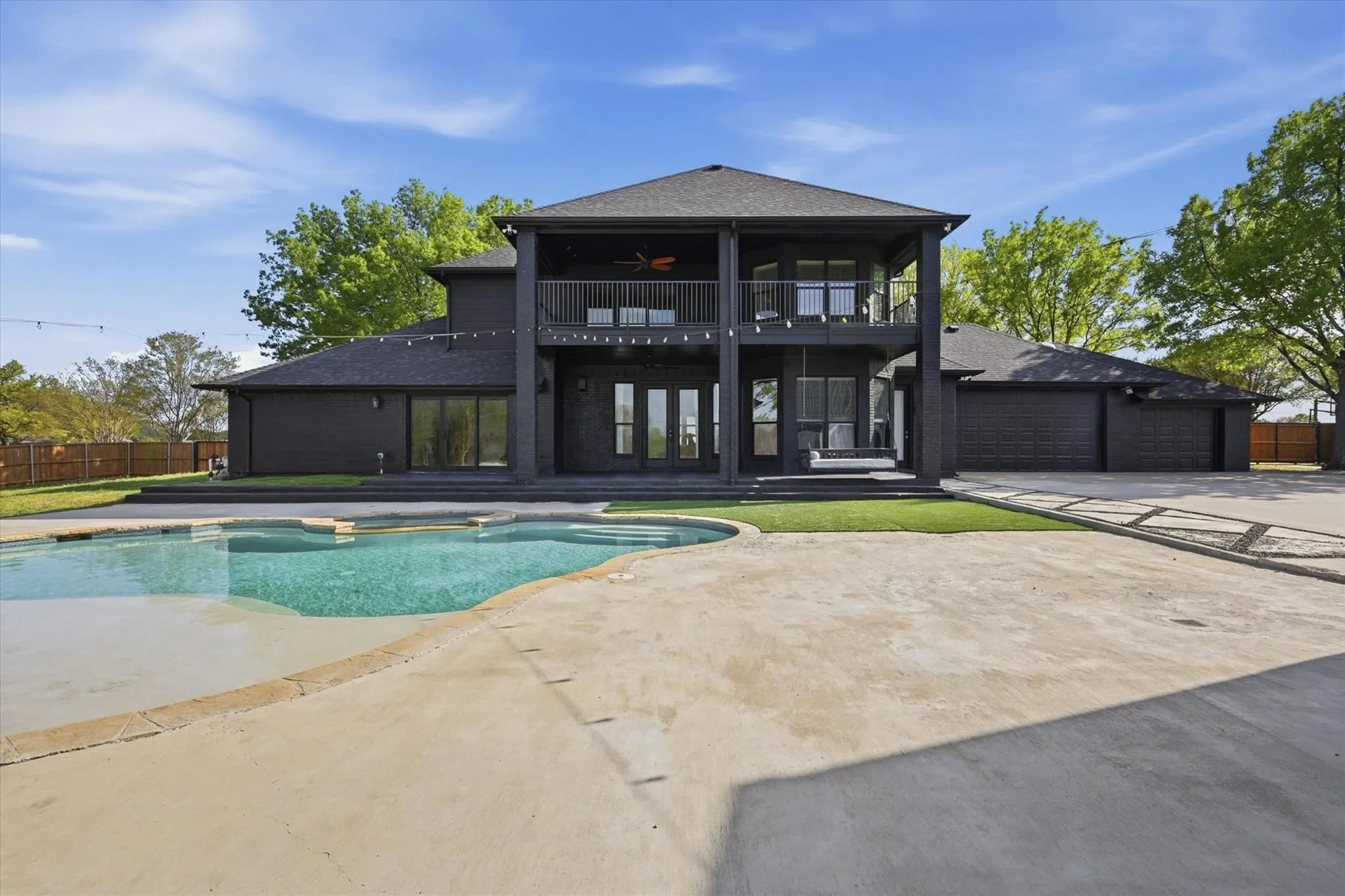 Two-story exterior with dark siding, featuring a covered balcony, lower patio, and an in-ground swimming pool