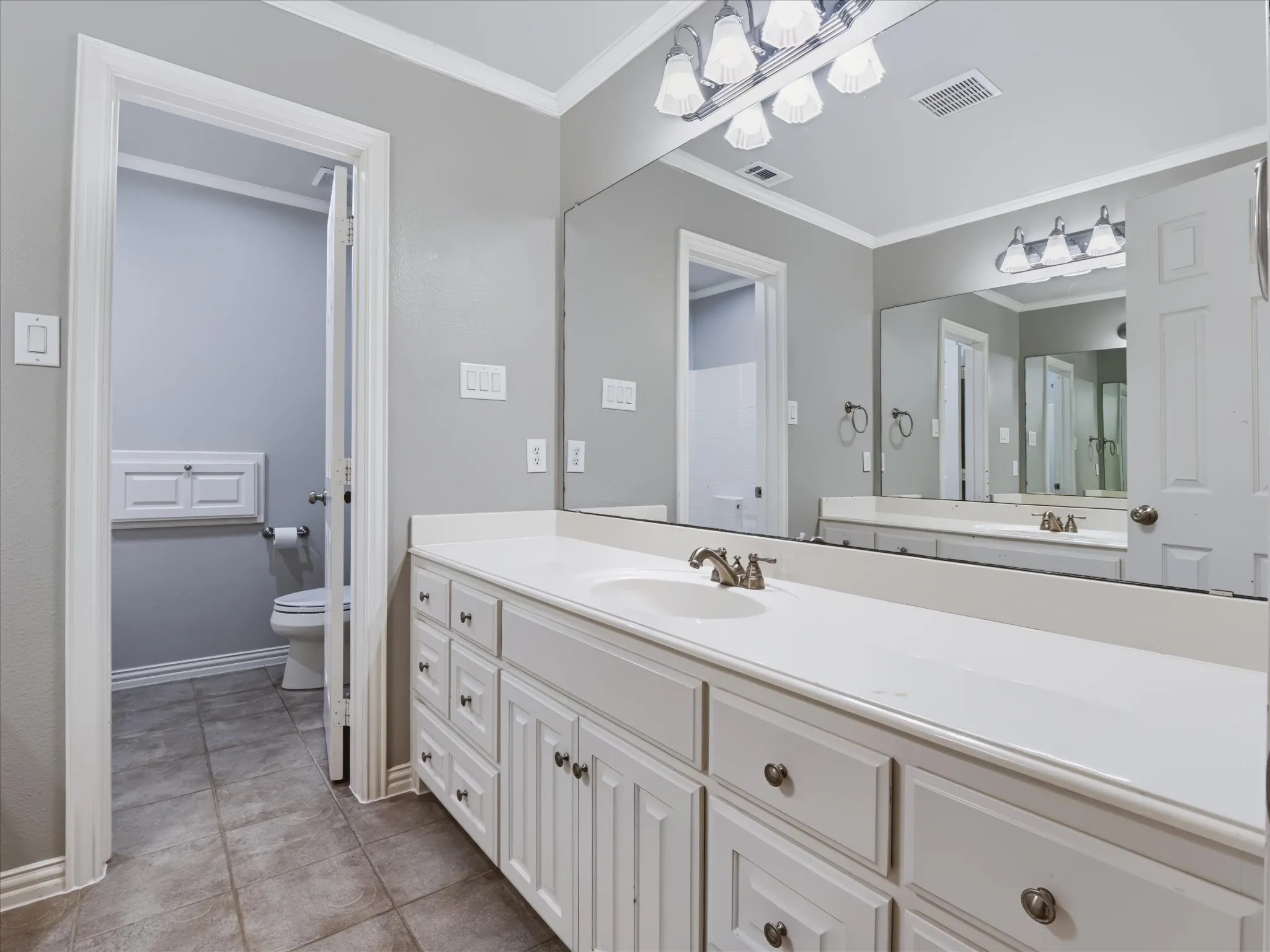 Extended vanity with dual sinks, white cabinetry, and a large mirror