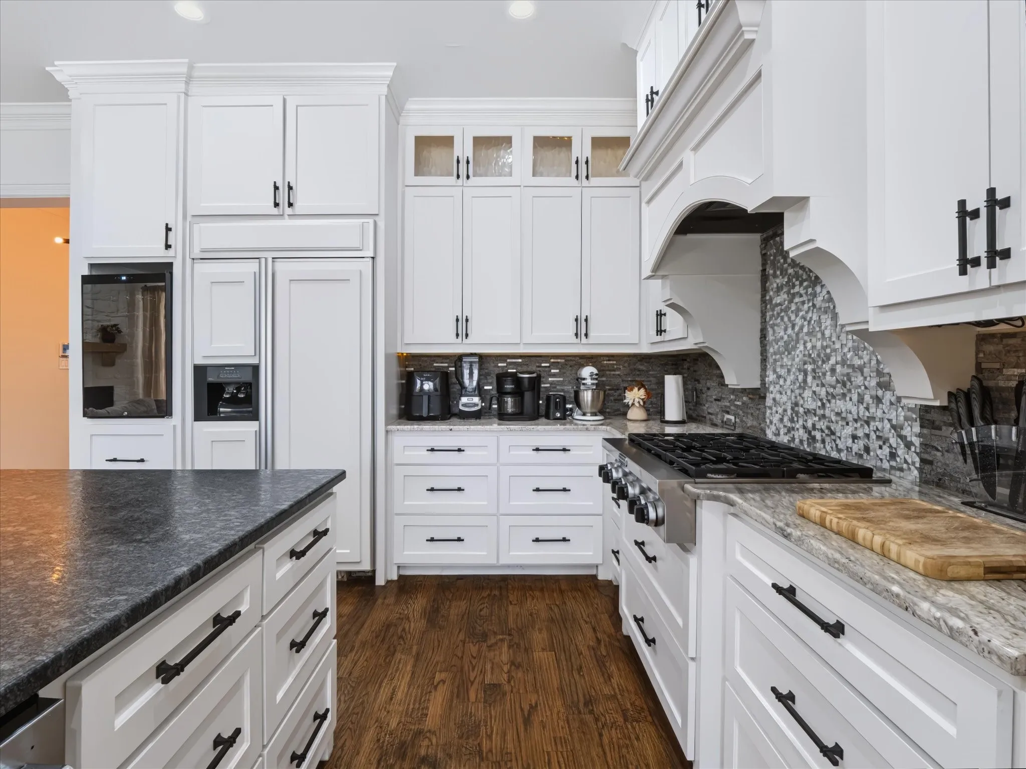 White cabinetry with matte black hardware, stainless steel gas range, tiled backsplash, and wood-finish flooring