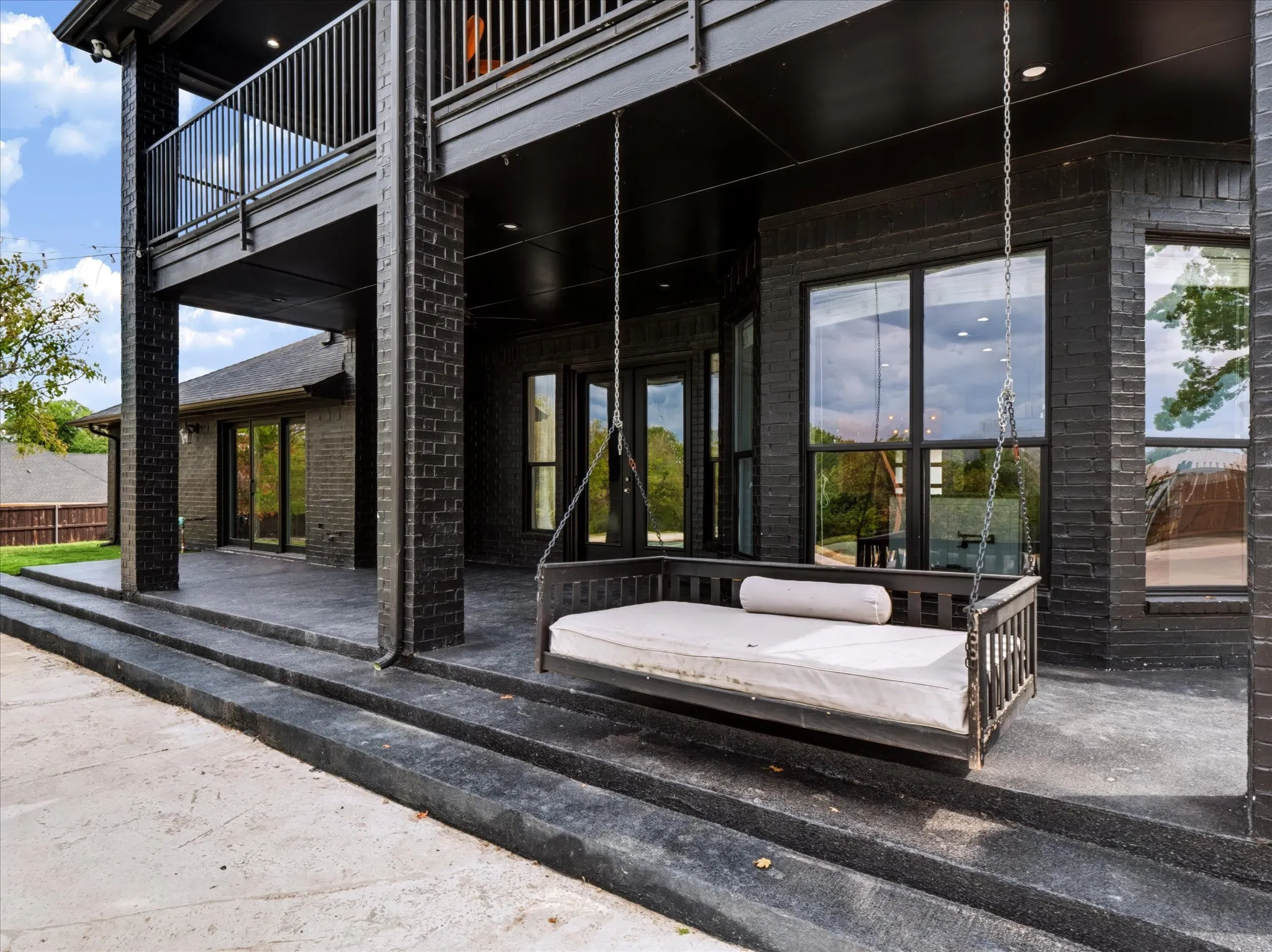 Covered patio featuring black brick columns and a suspended balcony with black railing