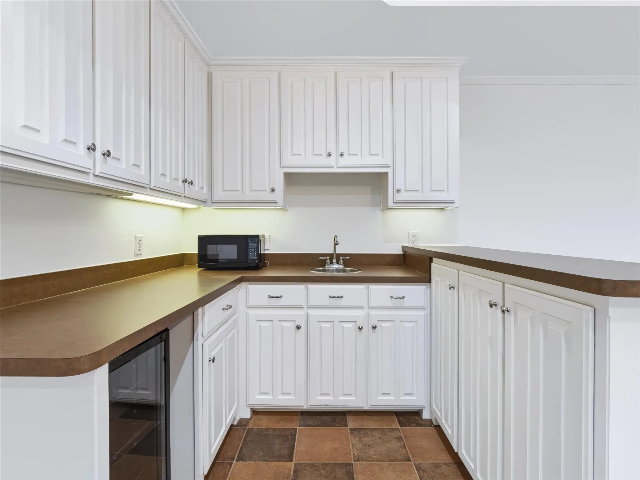 White shaker-style cabinetry, a built-in sink, under-cabinet lighting, a beverage refrigerator, and tile flooring