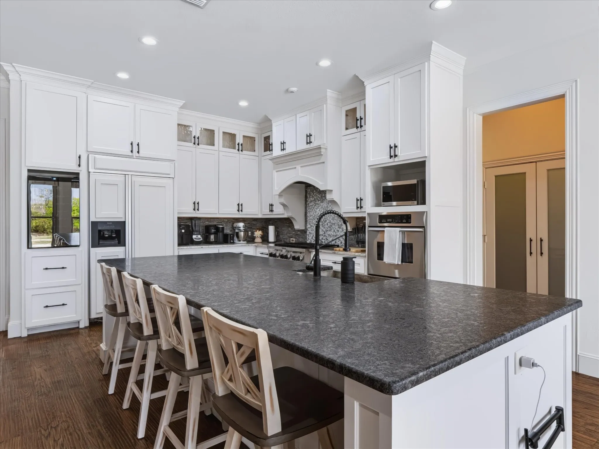 Spacious kitchen featuring an expansive island with a dark stone countertop, white shaker cabinetry, stainless steel appliances, and wood-finish flooring